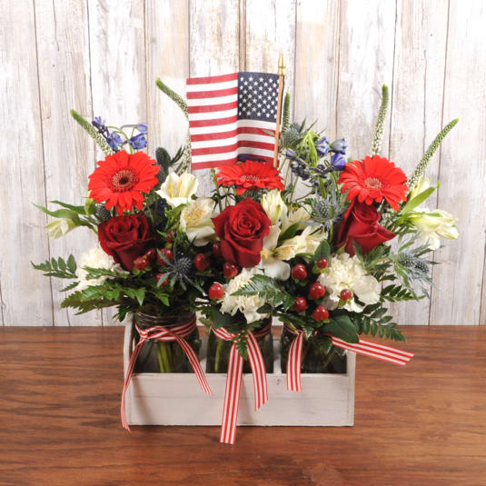 Patriotic red, white, and blue flower arrangement in mason jars with a small American flag.
