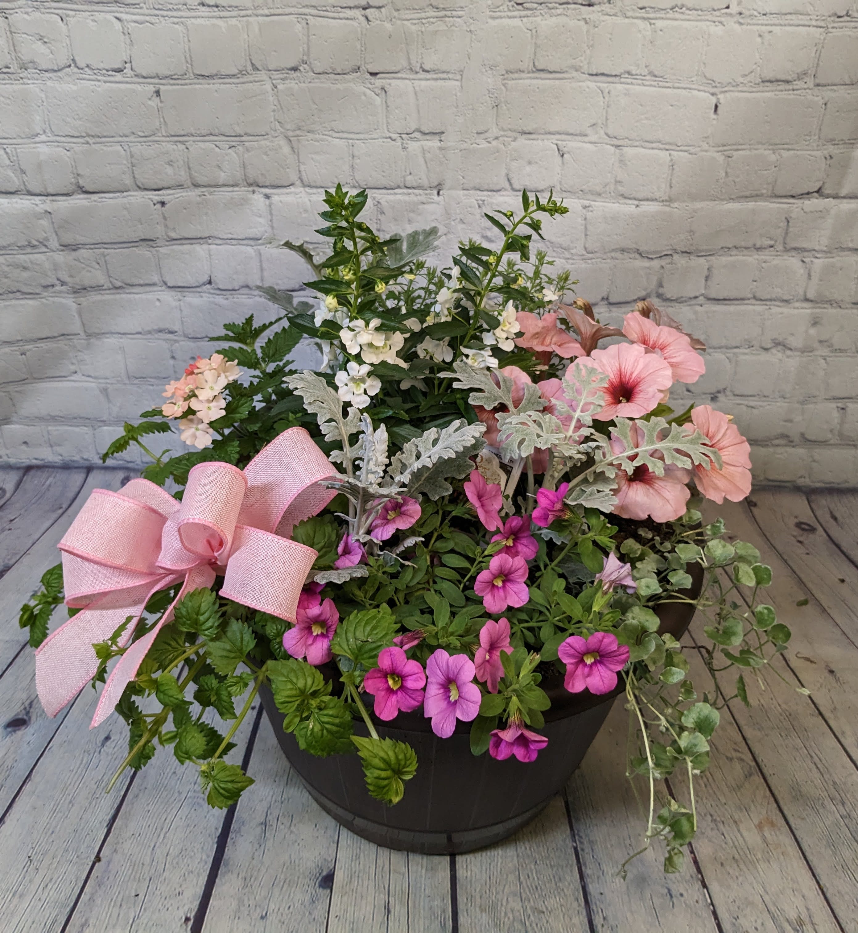 Mixed pink and white flowers in a black planter with a pink bow