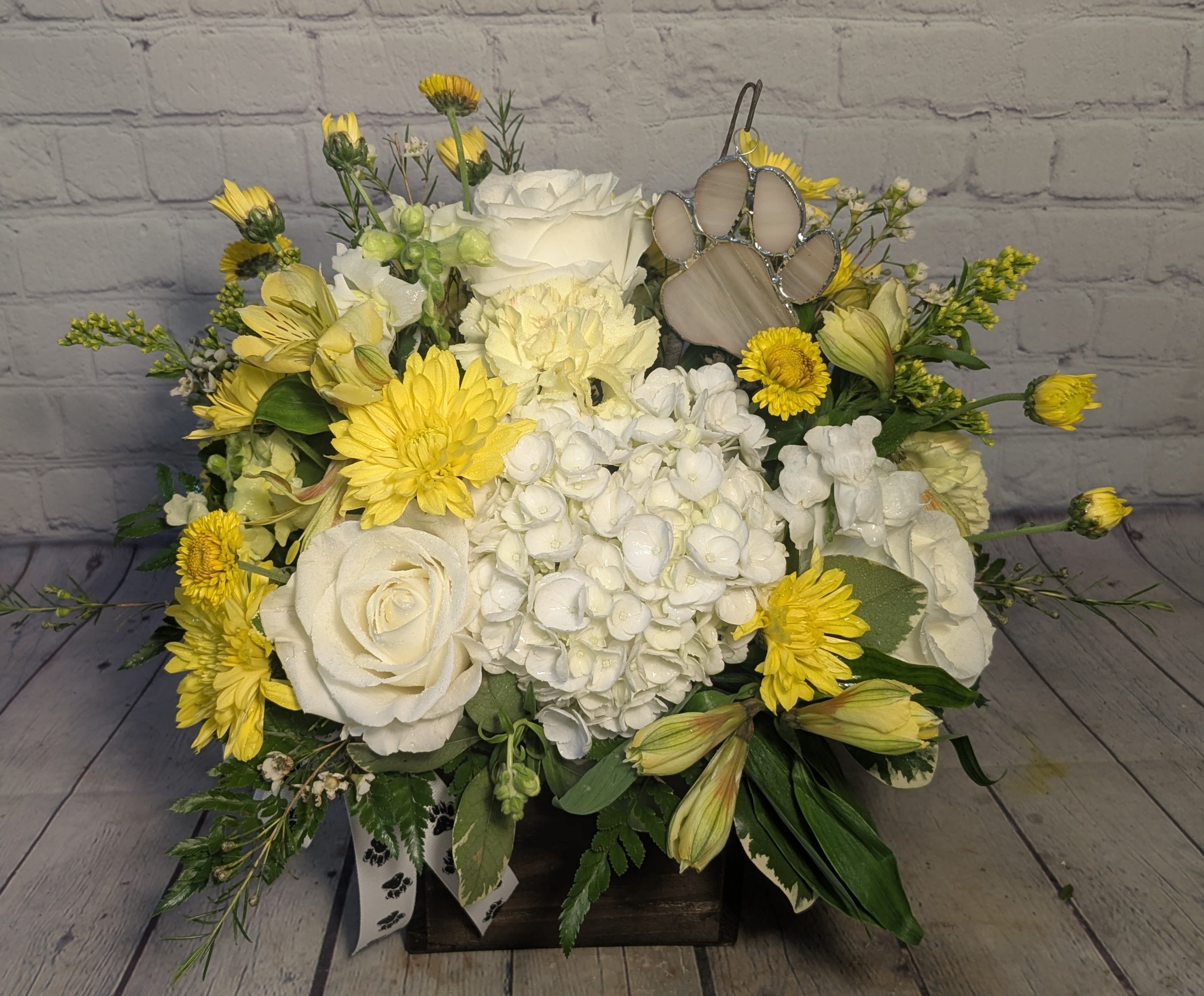 Paws &amp; Petals - Honor the memory of a beloved pet with our Paws in Heaven arrangement. This beautiful display features fresh yellow and white blooms, symbolizing peace, comfort, and cherished memories. Nestled among the flowers is a handcrafted stained glass paw print, made in our very own stained glass studio—a lasting keepsake to treasure forever. Presented in a rustic wooden cube, this heartfelt tribute offers a gentle reminder of the love and joy your pet brought into your life.