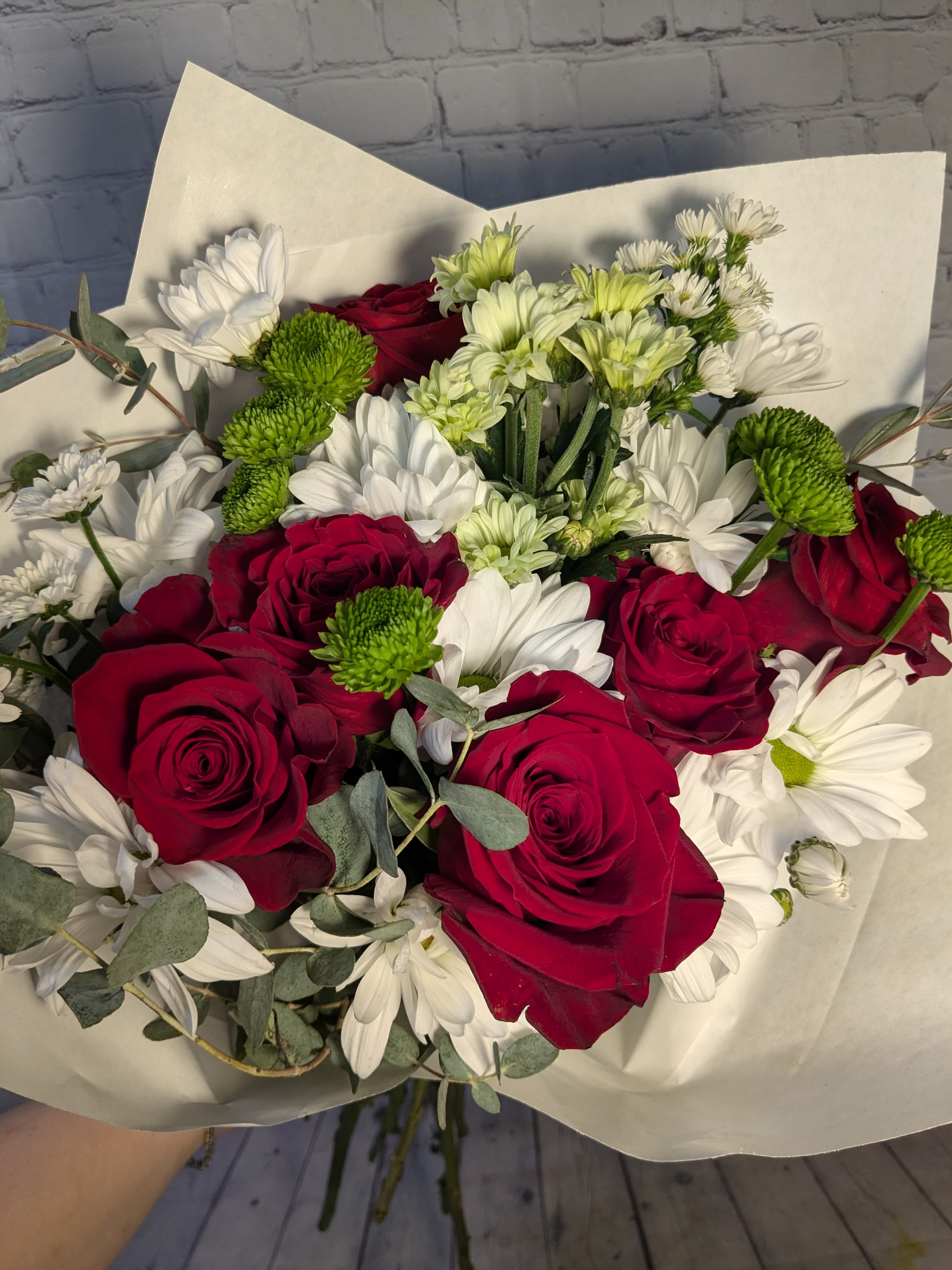 The Classic Hand-tied Bouquet - This classic bouquet is filled with Rosaprima red roses and accented with quaint daisies, chrysanthemums, micro daisies, &amp; eucalyptus. Allow this bouquet to convey what's on your heart and to speak when you don't have the words. *This is a hand-tied &amp; wrapped bouquet - not a vased arrangement. 