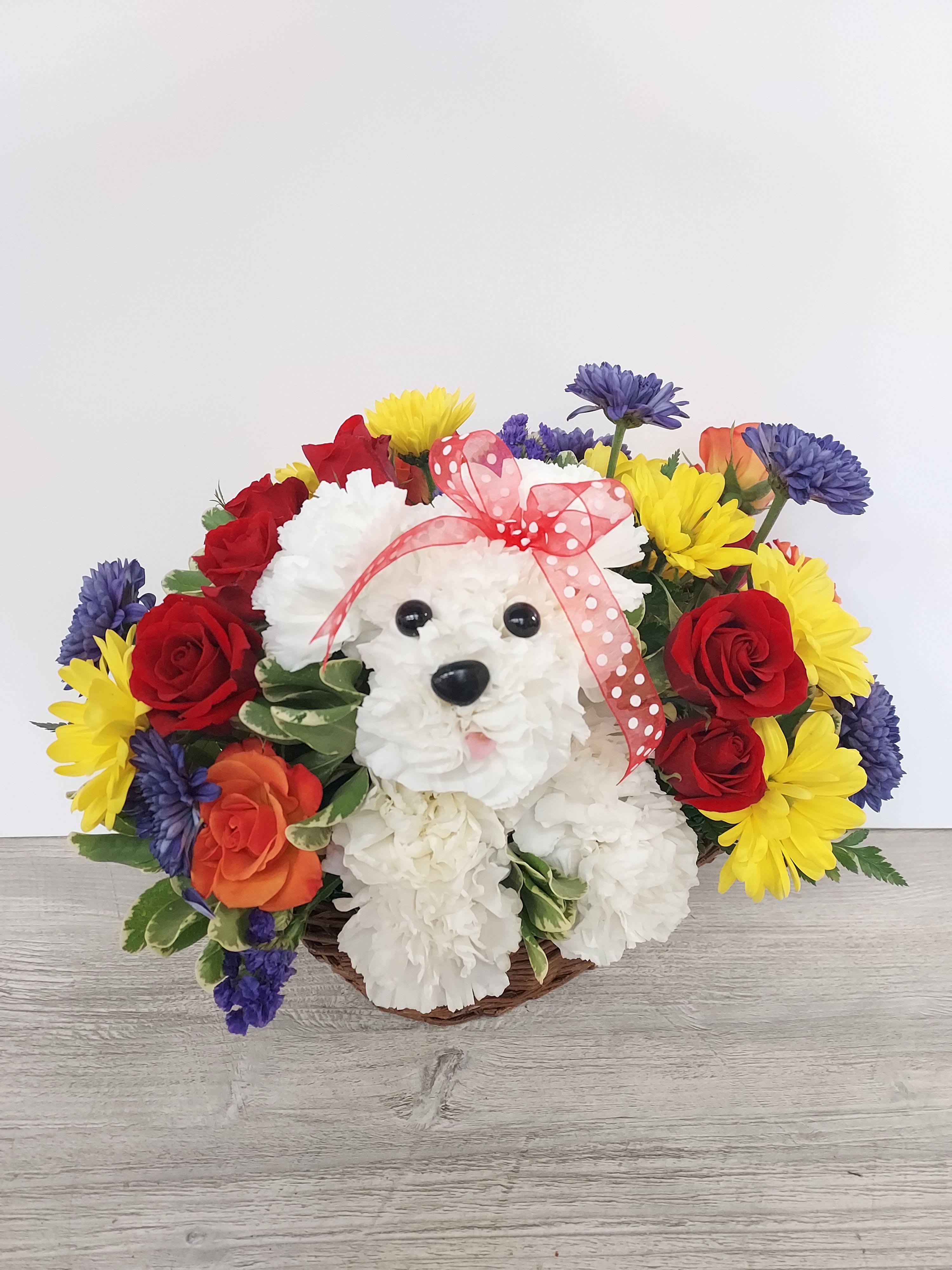 Basket arrangement with a white carnation dog surrounded by colorful flowers.