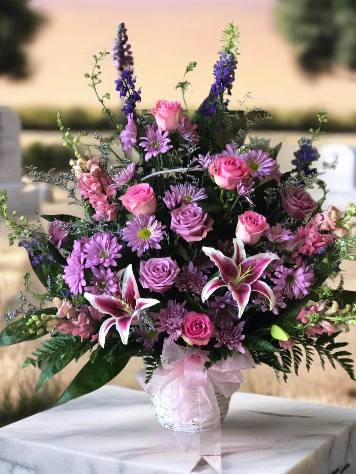 Pink and purple mixed flower arrangement in a white basket with ribbon