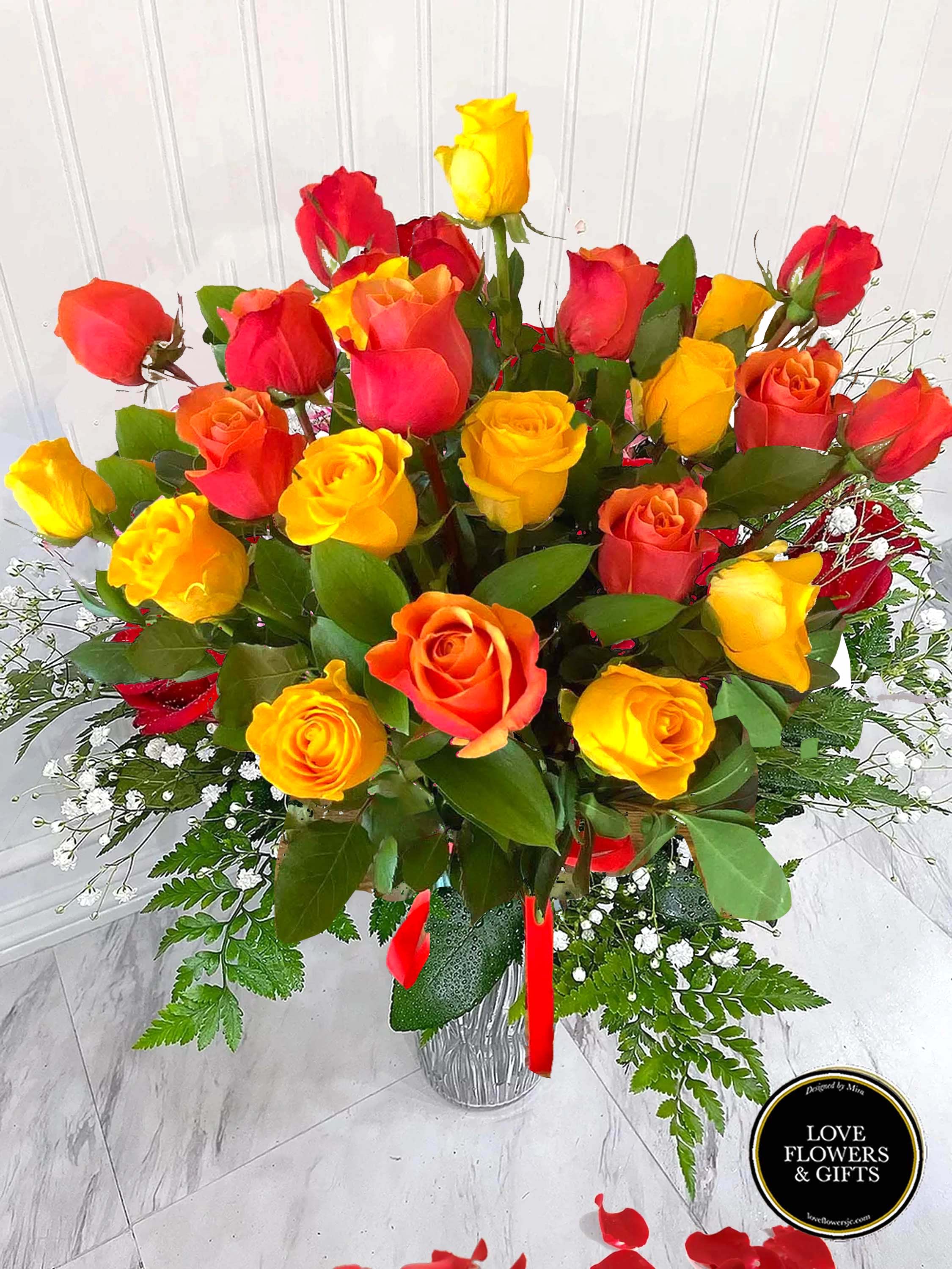 Tall arrangement of red, orange, and yellow roses in a clear glass vase