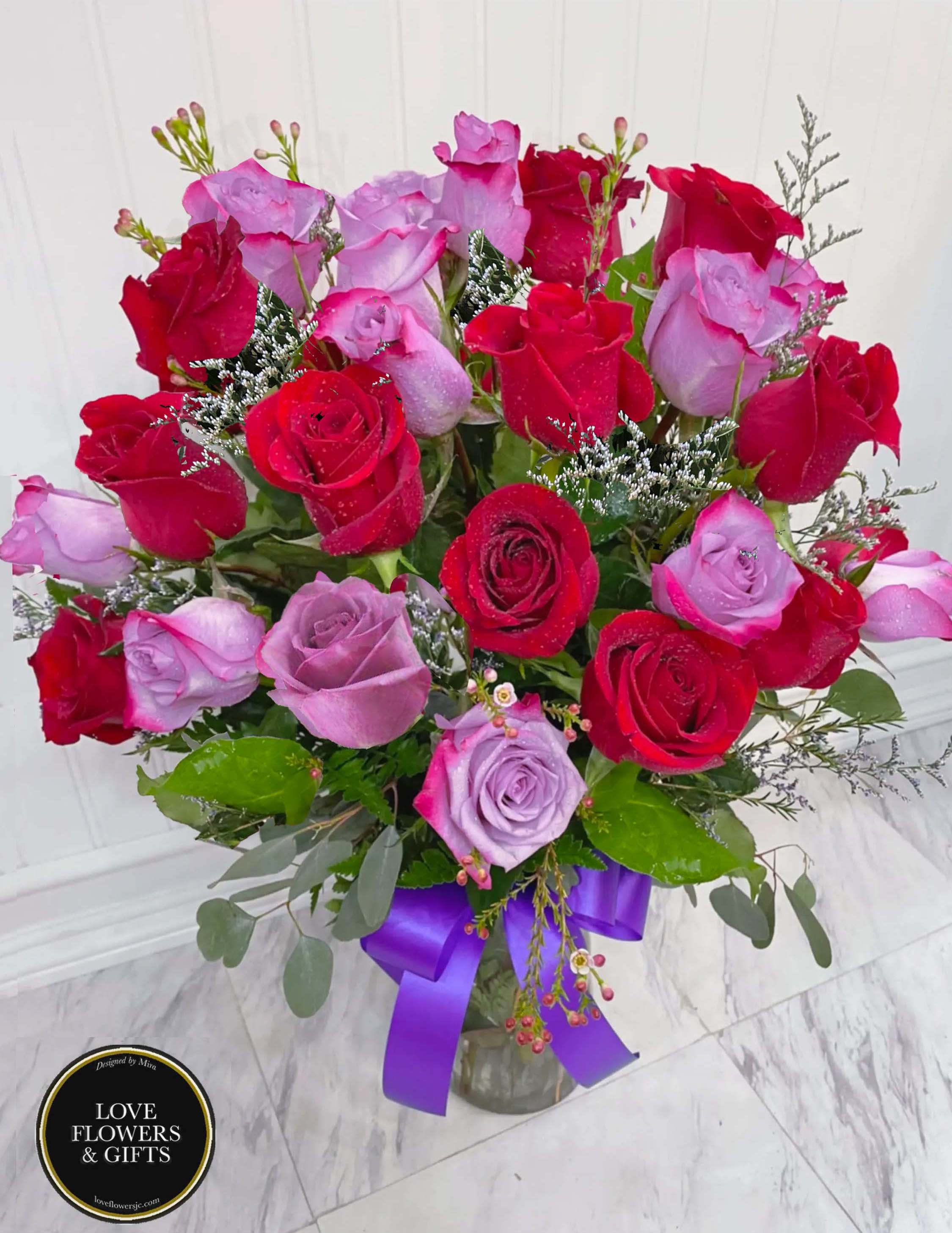 Arrangement of red and lavender roses in a clear vase with a purple ribbon bow