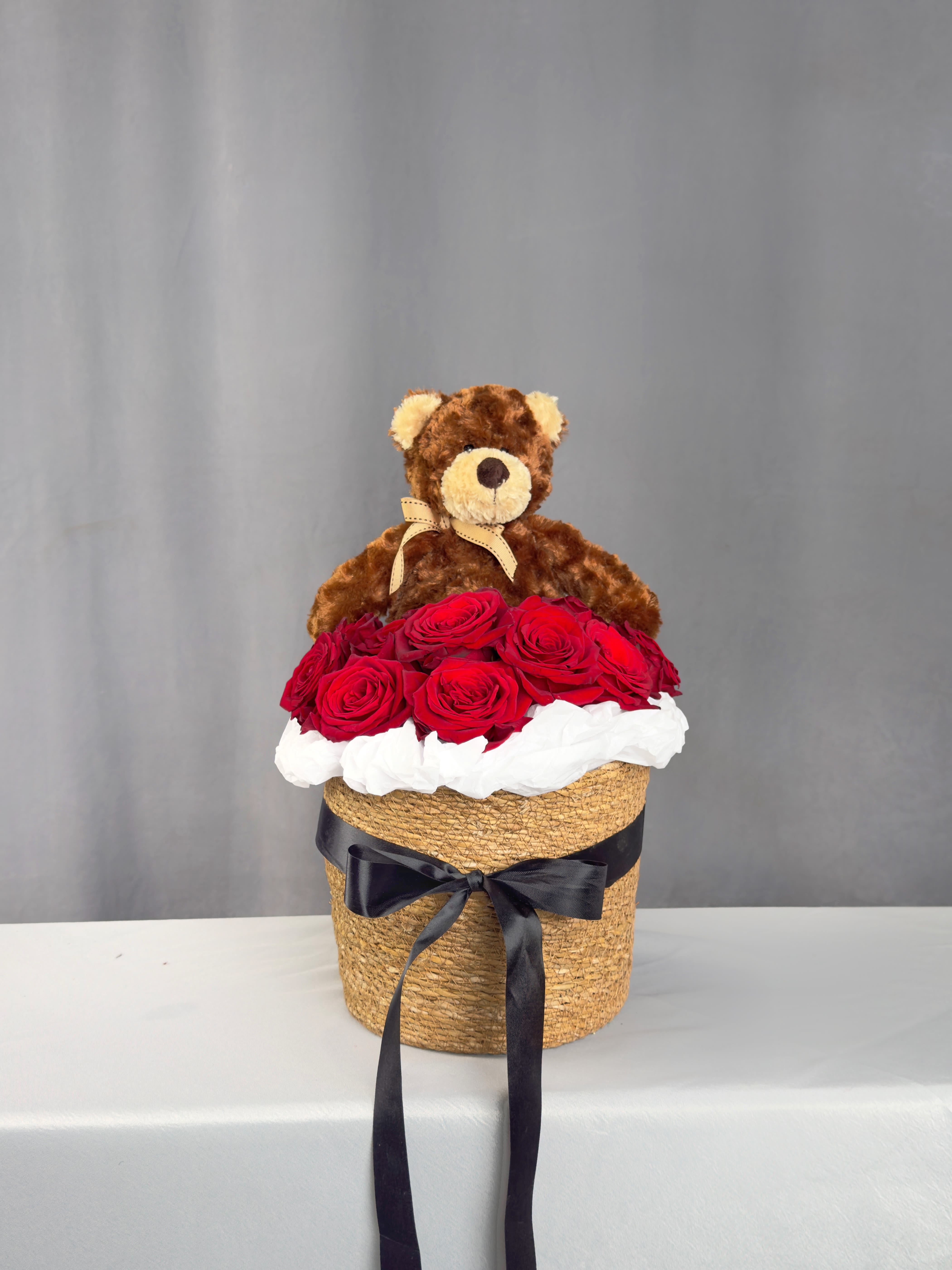 Teddy bear sitting on a box of red roses with a black ribbon