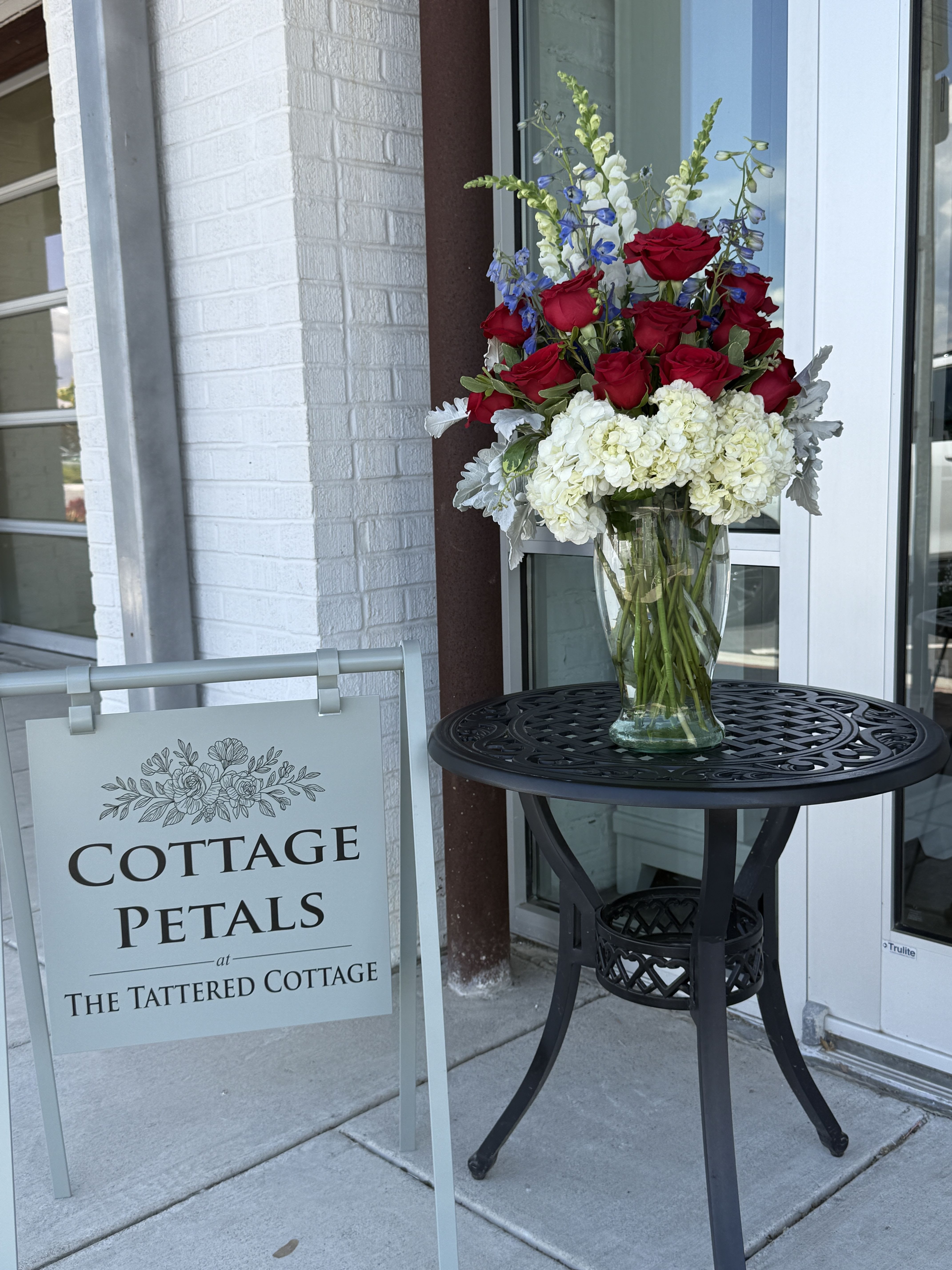 Honor &amp; Grace Tribute - A beautiful expression of remembrance and respect, the Honor &amp; Grace Tribute features rich red roses, crisp white hydrangeas, soft blue accent blooms, and fresh greenery thoughtfully arranged in a clear glass vase. Designed to symbolize love, honor, peace, and lasting memories, this elegant arrangement offers comfort during times of loss while serving as a meaningful tribute to a life well lived.  Its classic red, white, and blue palette makes it especially fitting for honoring veterans, active service members, first responders, or anyone remembered for their strength, dedication, and grace.  Flower varieties and accent blooms may vary slightly based on seasonal availability, but the overall style, fullness, and color palette will always be maintained.