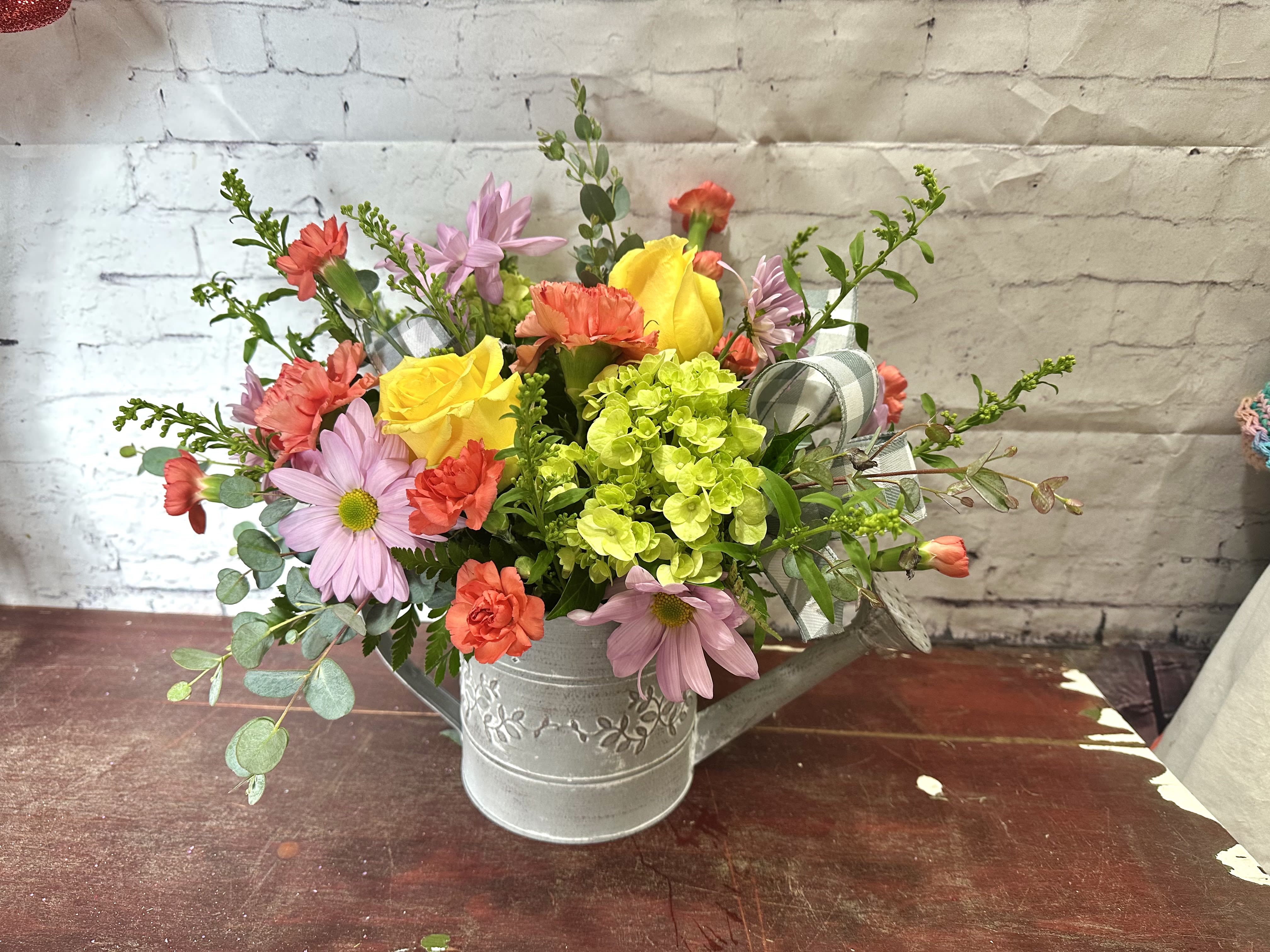 Mixed bouquet in a metal watering can with pink, yellow, and coral flowers