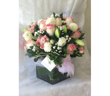 Pink and white bouquet in a square glass vase with a pink ribbon