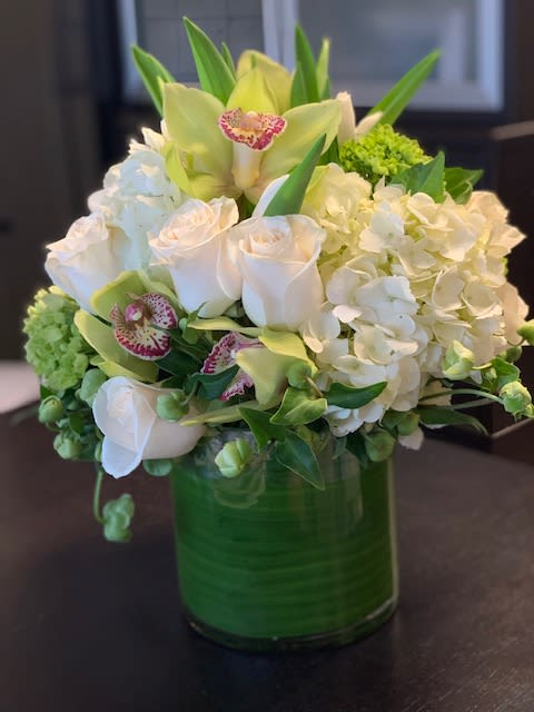 White roses, hydrangeas, and orchids in a green glass vase