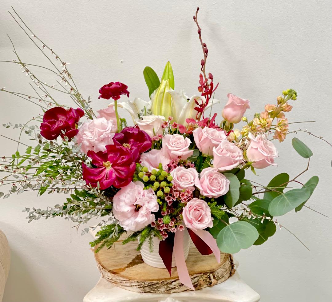 Pink and red floral arrangement in a white container with lilies and roses