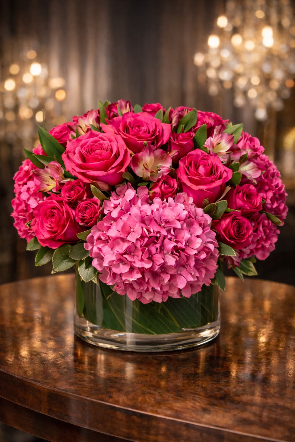 Fuchsia Desire - A bold and romantic luxury arrangement featuring premium hot pink roses, lush hydrangea, and elegant accent blooms arranged in a modern glass cylinder vase. Designed in rich shades of fuchsia and deep pink, this piece is full, textured, and beautifully balanced. The vibrant roses create depth and romance, while the hydrangea adds softness and volume for a dramatic yet elegant presentation. Perfect for anniversaries, romantic gestures, birthdays, Valentine’s Day, or making a powerful statement of love. • Premium hot pink roses • Lush pink hydrangea • Accent blooms &amp; fresh greenery • Modern glass cylinder vase included • Full, rounded luxury design This arrangement is handcrafted for maximum fullness and visual impact. ⸻  Seasonal &amp; Freshness Guarantee We carefully select the freshest blooms available to ensure vibrant color and long-lasting beauty. Because flowers are seasonal and market availability may vary, certain accent blooms or greenery may occasionally be substituted. If substitutions are necessary, we will: • Maintain the same pink/fuchsia color palette • Preserve the same full, rounded luxury style • Keep the same overall size and premium value • Use flowers of equal or greater quality Your arrangement will always reflect the same bold, romantic aesthetic shown — never a different theme or reduced design. Each piece is handcrafted with attention to balance, density, and elegance.