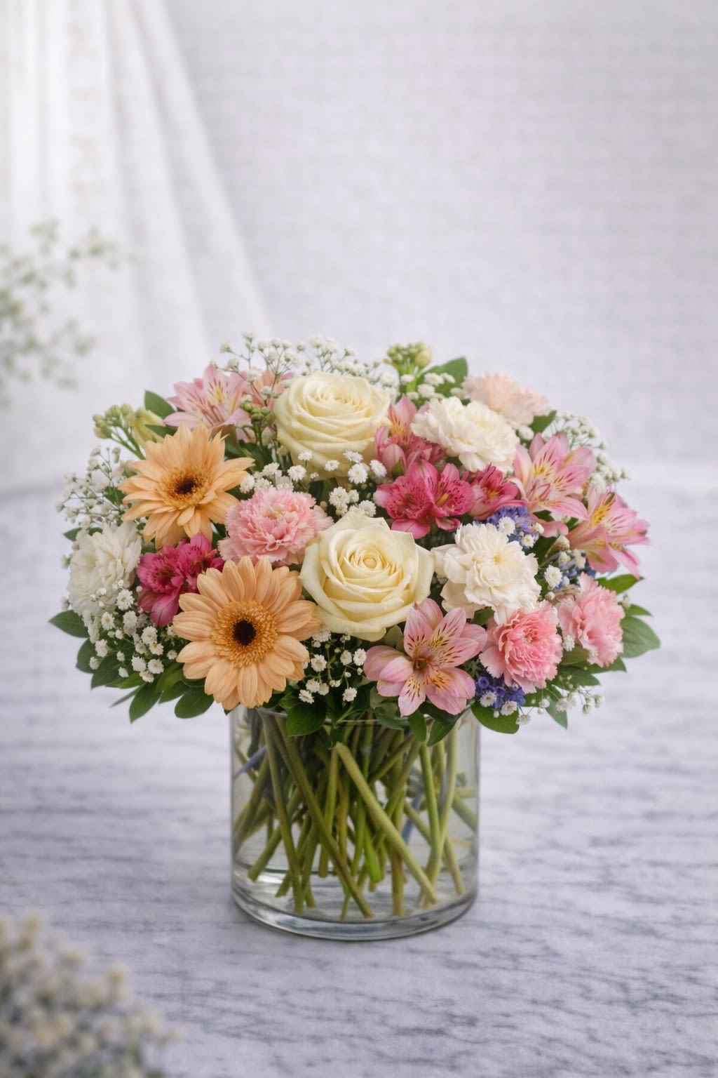 Golden Blush Garden - Golden Blush Garden is a soft and elegant arrangement designed in warm peach, blush pink, and creamy ivory tones. Featuring a beautiful blend of roses, gerbera daisies, alstroemeria, carnations, and delicate accent blooms, this design brings a fresh garden-inspired feel to any space. Arranged in a clear glass vase, the stems are beautifully visible for a clean and timeless look. Please note: Flower varieties may vary depending on seasonal availability. When substitutions are necessary, we carefully select blooms of equal or greater value while maintaining the same color palette and overall style. Containers may vary slightly in texture or shape but will always complement the arrangement’s colors and design. The overall look, color scheme, and feel of the arrangement will always remain consistent with the photo. 