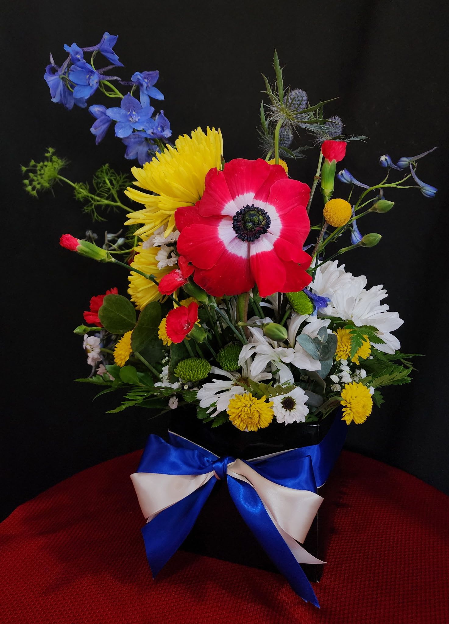 For the Bad Ass Dad - A special arrangement dedicated to all the amazing fathers out there who do so much for their families. The box and the oasis foam inside is bio-degradable. This arrangement includes chrysanthemums, daisies, delphiniums, one anemone, carnations, queen anne's lace, thistle, pom pons, leather greens and dollar eucalyptus.  biodegradable box dimensions are approximately 5 1/2" H x 5 1/2" W x 5 1/2 " L. With flowers is approximately 19" H x 14" W x 14" L. 