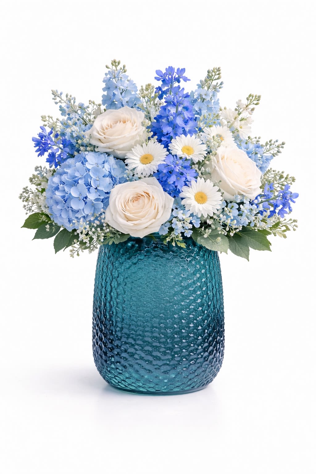 Ocean Breeze - Bring the calming beauty of the coast into any space with this fresh, ocean-inspired floral arrangement. Designed in a textured teal glass vase, this piece features a refreshing mix of white roses, soft blue hydrangeas, delicate daisies, and seasonal blue blooms. The cool tones and airy design create a serene, beachy vibe—perfect for birthdays, thank you gifts, or simply brightening someone’s day. Flower varieties may vary slightly based on availability while maintaining the same color palette and style.