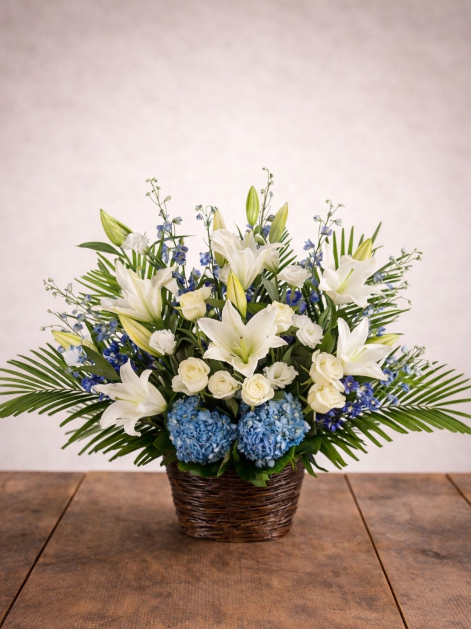 White lilies, roses, and blue hydrangeas in a wicker basket