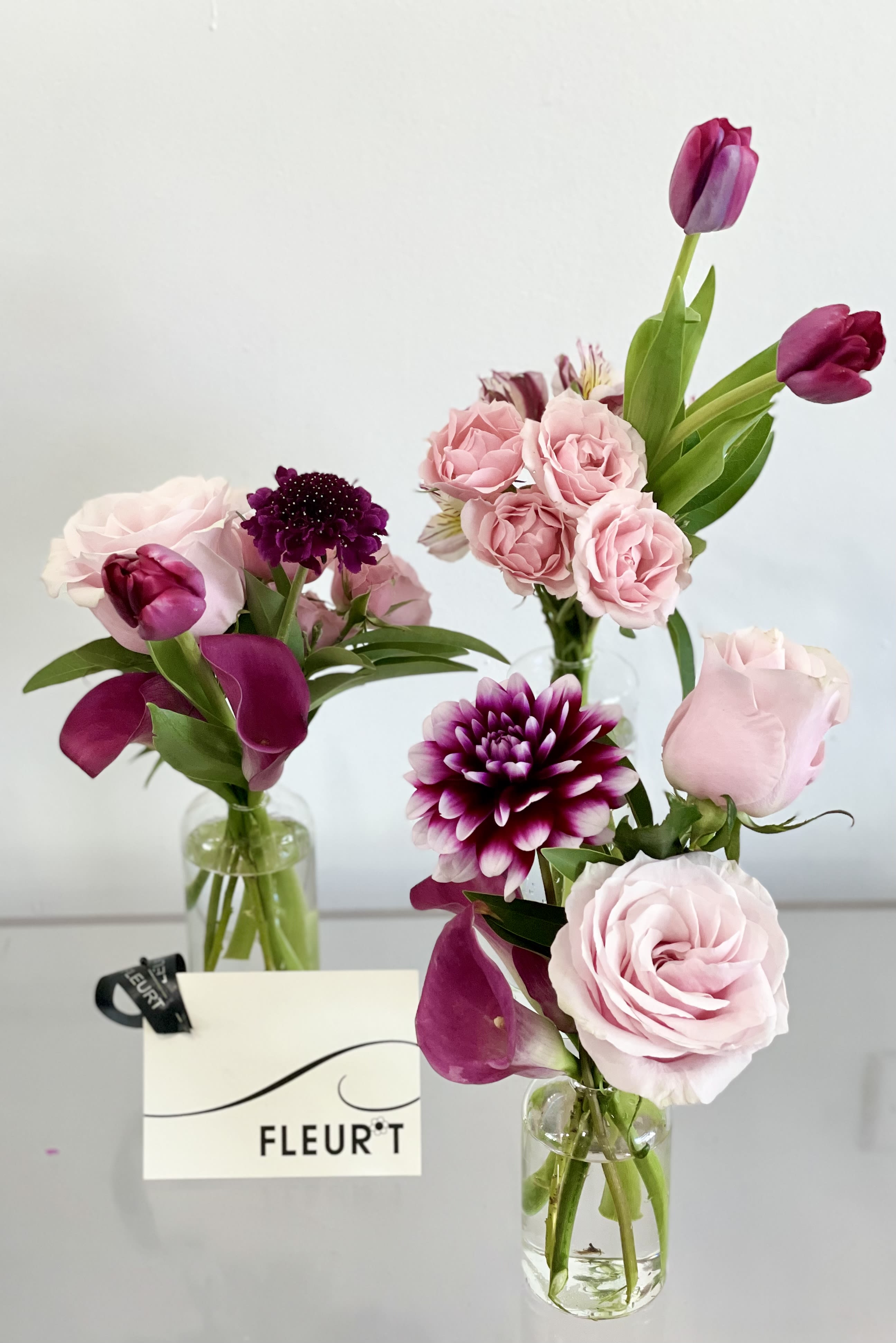 Pink rose and purple tulip arrangements in clear glass vases