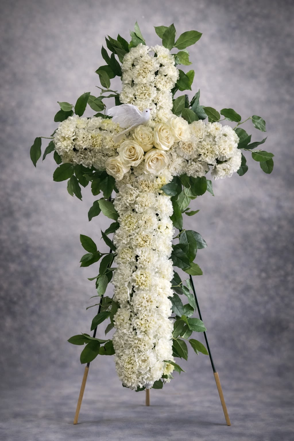 Peaceful Spirit Cross - A graceful standing cross designed with fresh white carnations and roses, accented with lush greenery and a symbolic white dove. This elegant tribute represents peace, faith, and eternal rest.  Displayed on an easel, this arrangement offers a comforting and spiritual presence at funeral services, memorials, and church ceremonies.  Substitutions may be necessary based on availability, but the overall cross shape, color palette, and fullness will always be maintained.  Delivery available to funeral homes, churches, cemeteries, and residences. Please include service time and location details at checkout.