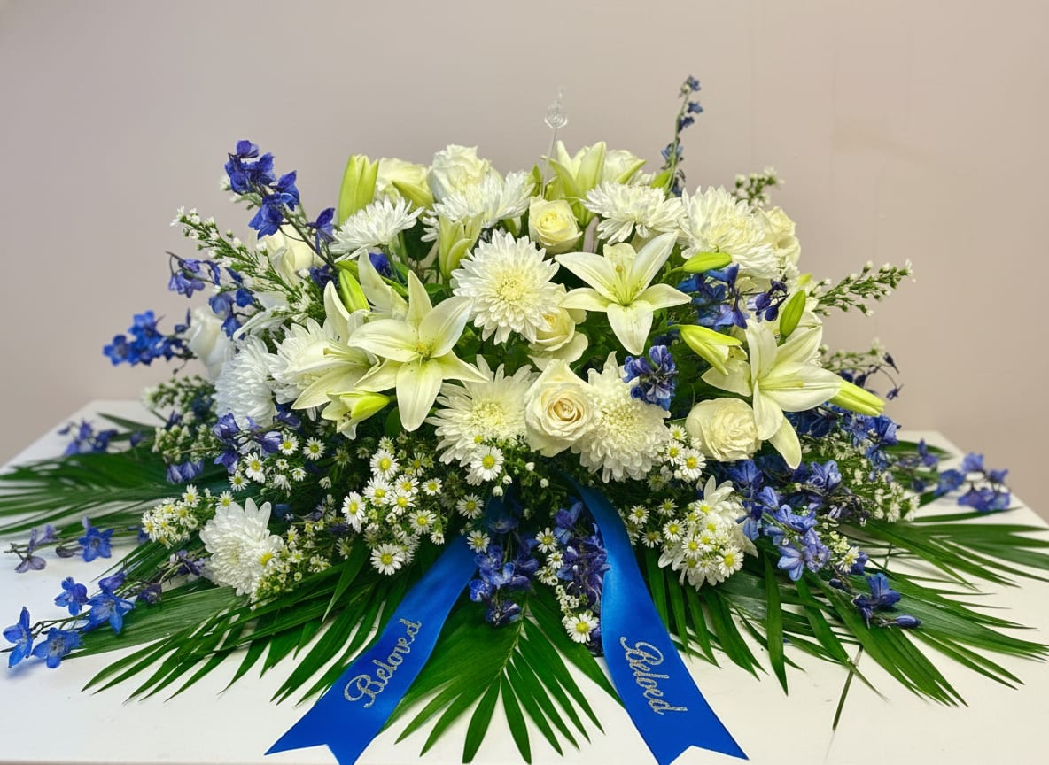 Cherished Memories - Blue and white half casket spray Spray contains white roses, lilies, wax flower, mums, blue delphinium and palm leaves