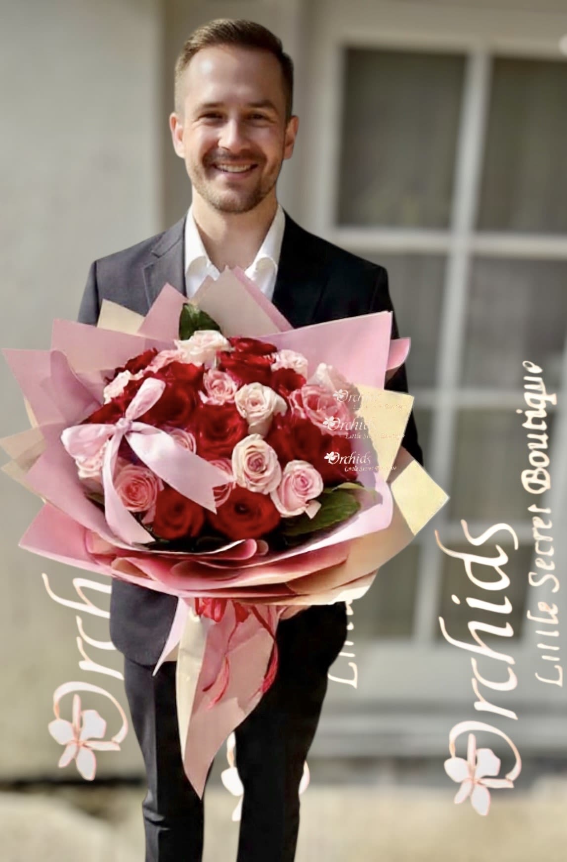 Man holding a large bouquet of red and pink roses wrapped in pink paper