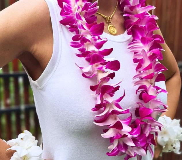 Woman wearing two magenta and white orchid leis over a white top.