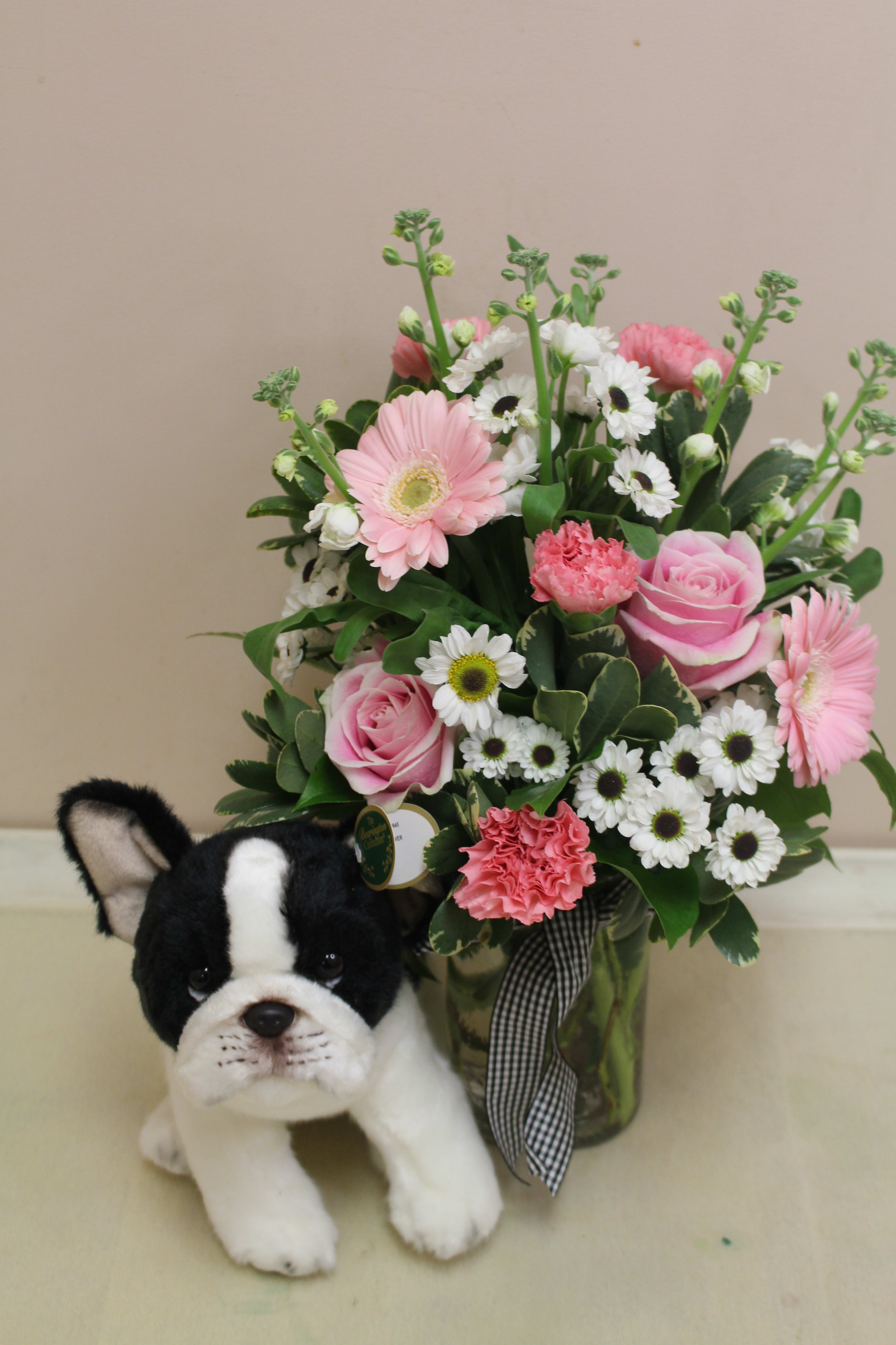 Pink and white flower arrangement with a plush dog in front