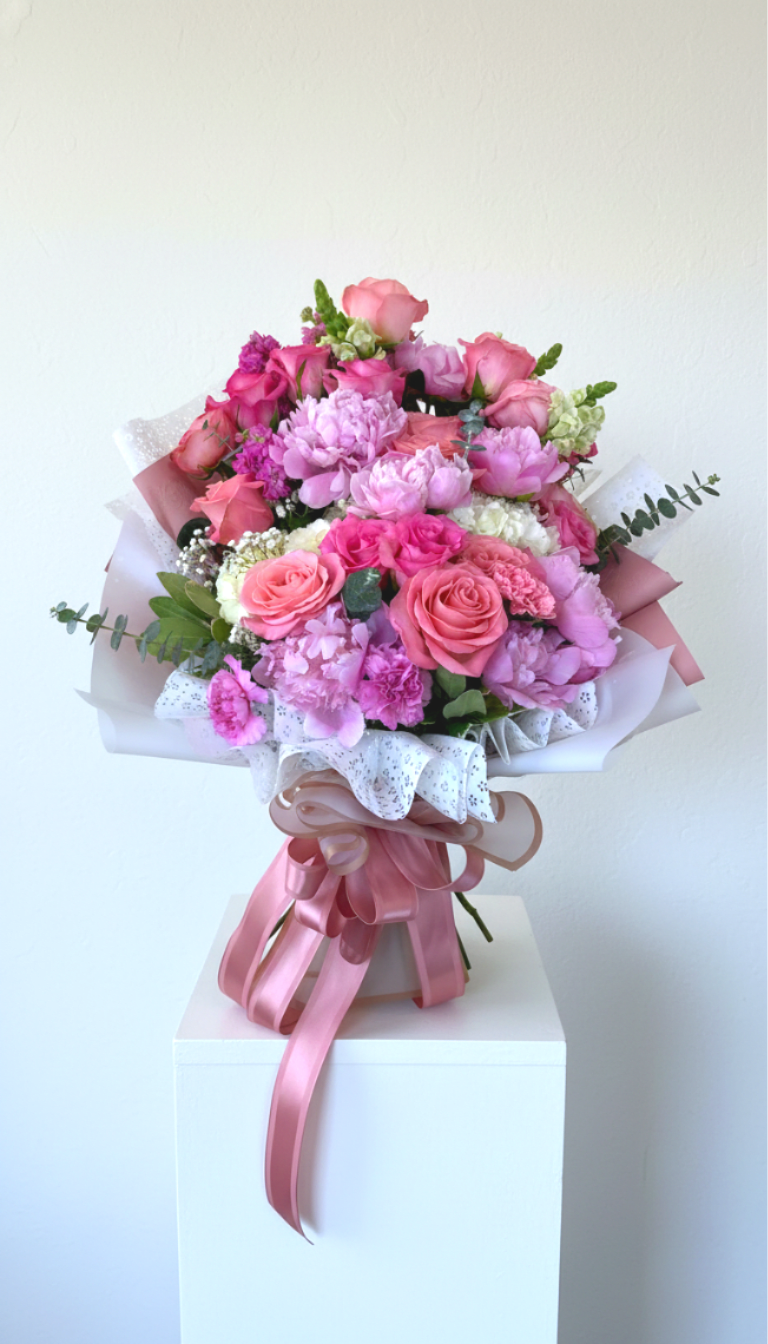 Darling of Mine - A lush, garden-style hand-tied bouquet overflowing with pink roses and layered peony-like blooms-this wrapped bouquet reads like a celebration in floral form.This is the PERFECT wrapped bouquet for literally any reason at all. She graduated? Done. She got that license? Perfect.  Need a pick-me-up? We got you. It's the kind of arrangement that makes the person you're thinking of feel genuinely seen: soft blush to deeper rose tones, pale lilac accents, and bright white filler blooms create a feminine, sentimental impression.  Carefully built in a full, rounded dome shape, the bouquet mixes roses, peony-like blooms, carnations, hydrangea touches and sprigs of eucalyptus for texture and contrast. Finished with embossed and textured decorative paper, clear bouquet wrap and a wide satin ribbon, the presentation is polished and gift-ready. The designer-sized arrangement is generously proportioned-literally the size of a torso-and uses premium conditioned florals for lasting freshness.  Available for local delivery or pickup in Northwest San Antonio; call us to let us know of any special instructions so your recipient gets the full grand-statement experience.