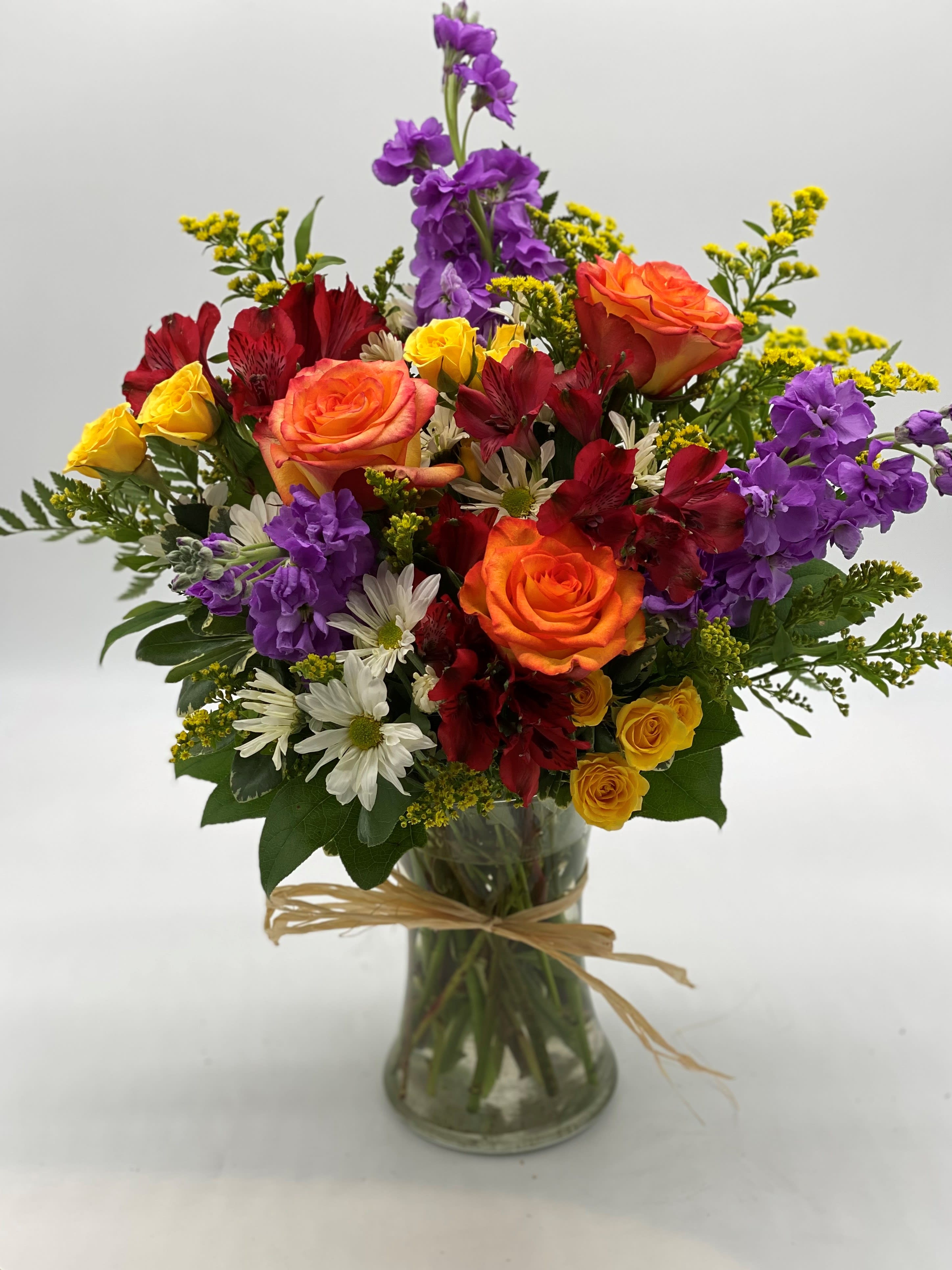 Mixed bouquet of roses, purple stock, and white daisies in a glass vase