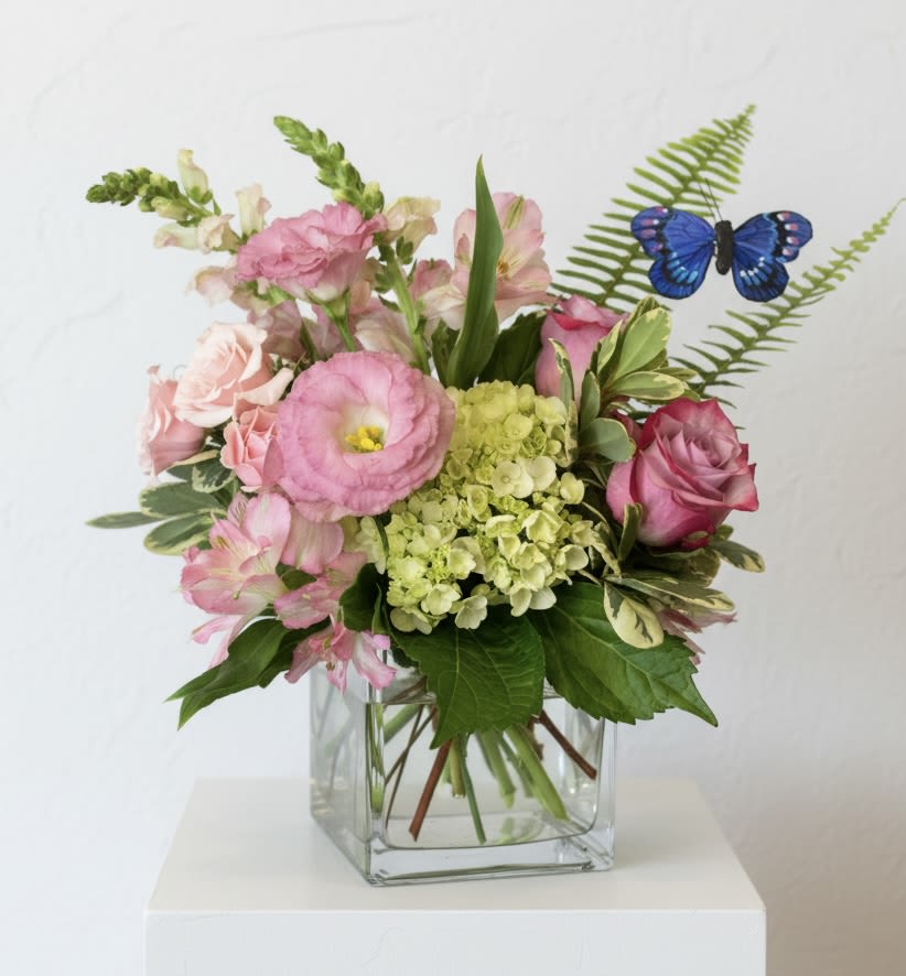 Butterfly Kisses - A sweet cube vase arrangement filled with roses, lisianthus, hydrangea, snapdragons and premium accent flowers and foliage. A “flutterby” adds a bit of whimsy to the design.