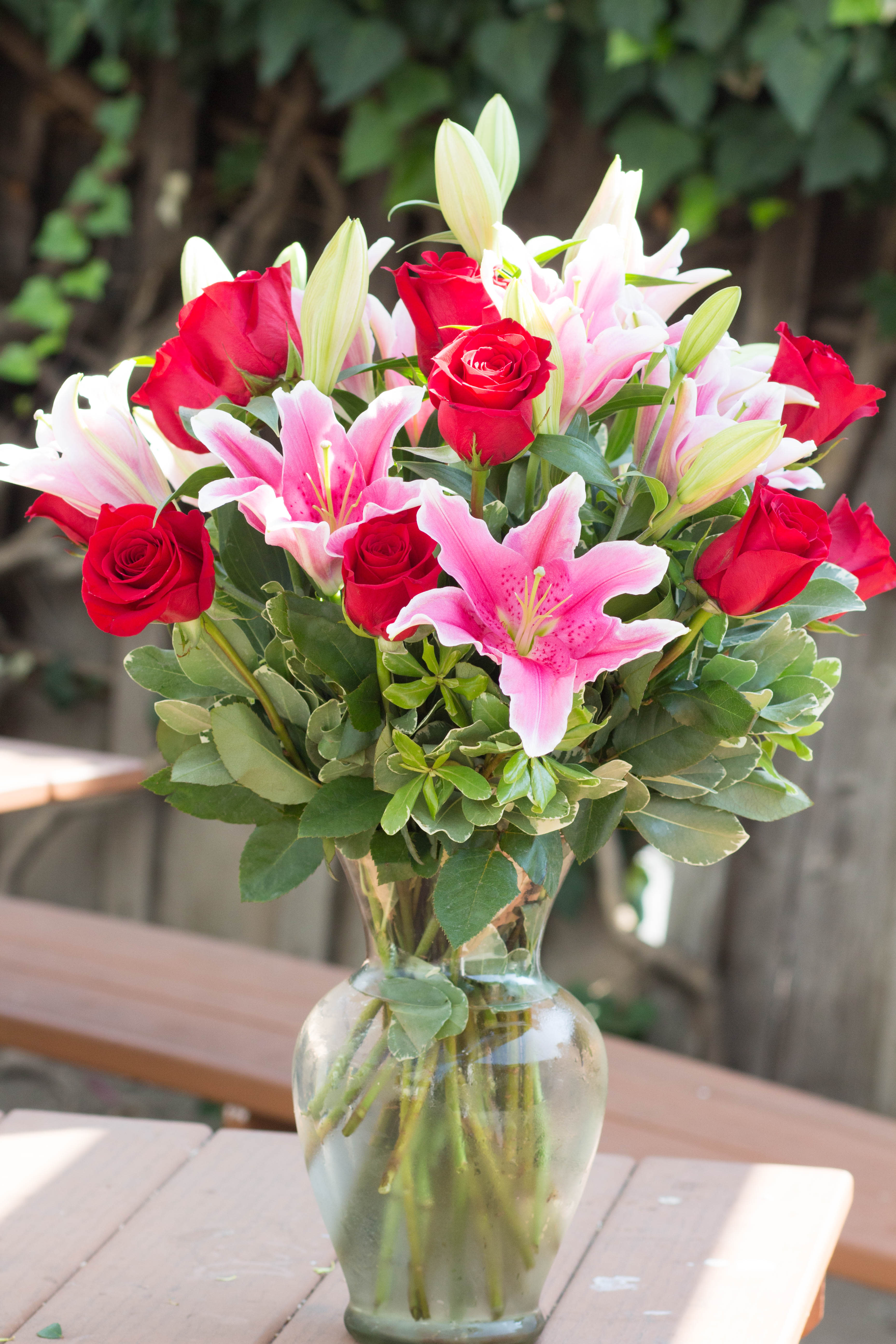 Bouquet of red roses and pink lilies in a clear glass vase
