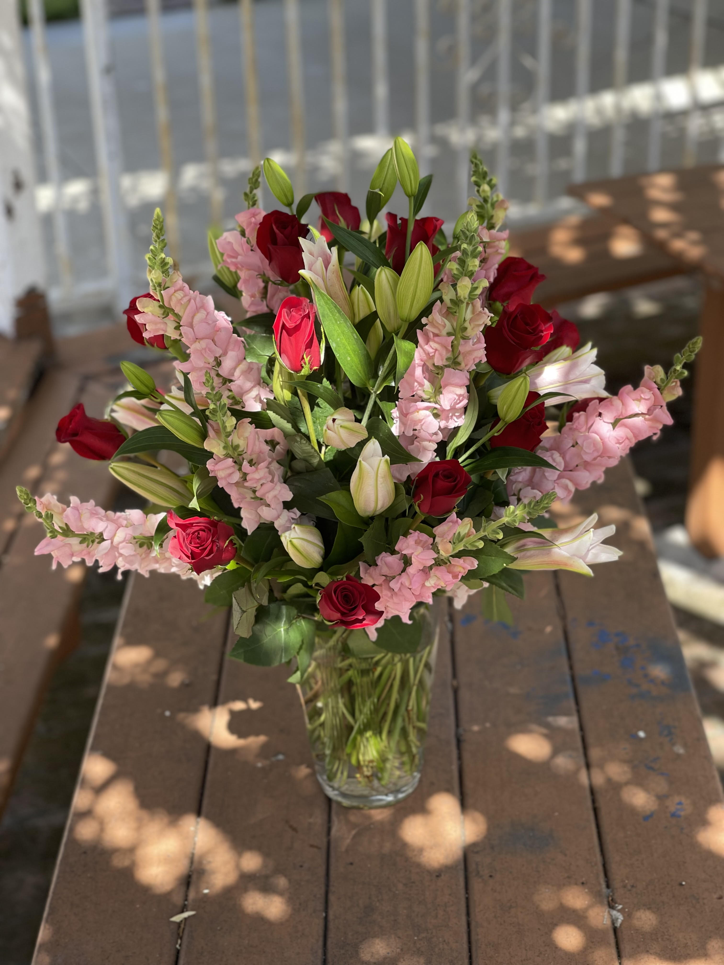Bouquet of red roses, pink snapdragons, and white lilies in a glass vase