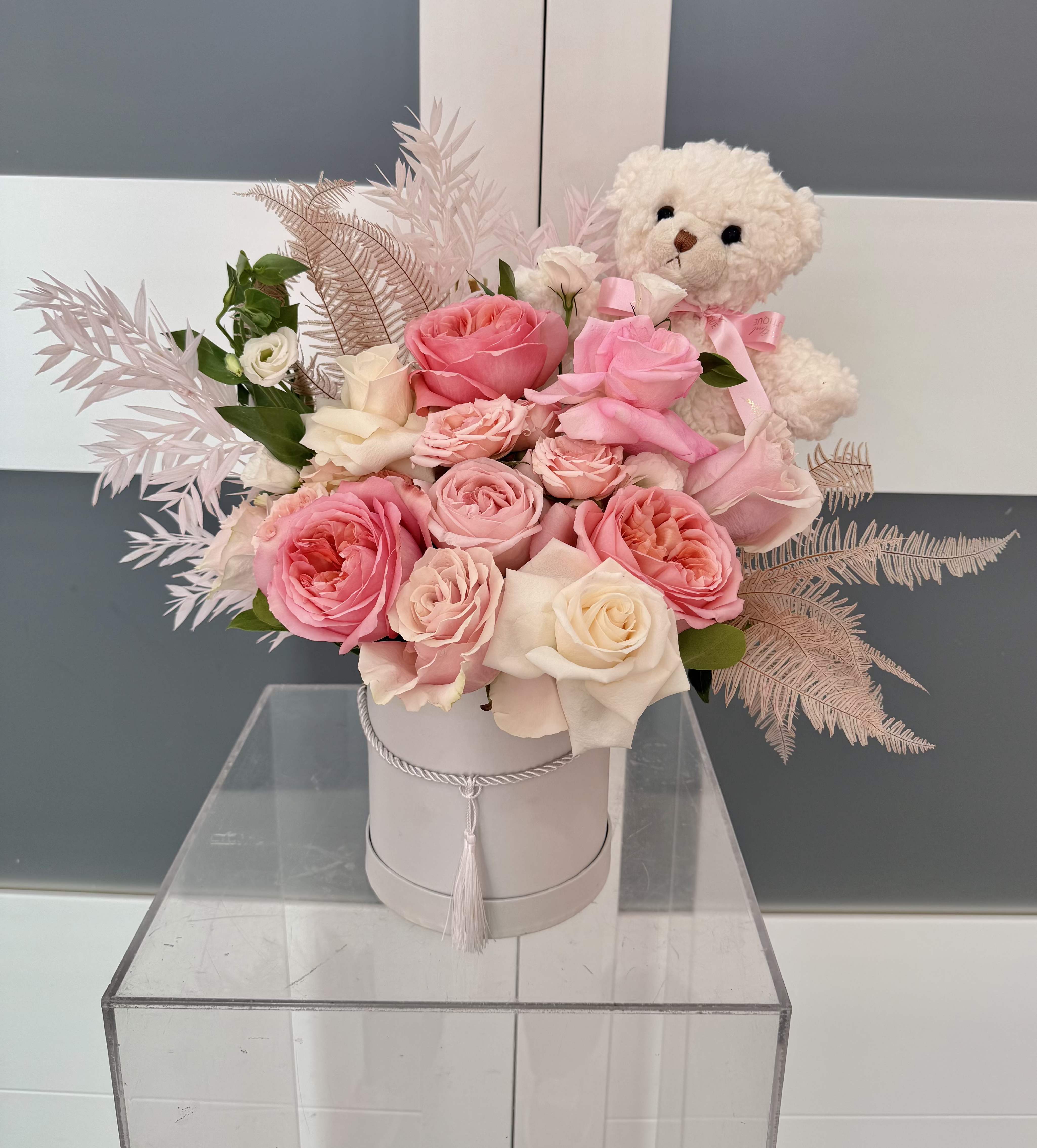 Pink and white roses in a round box with a teddy bear