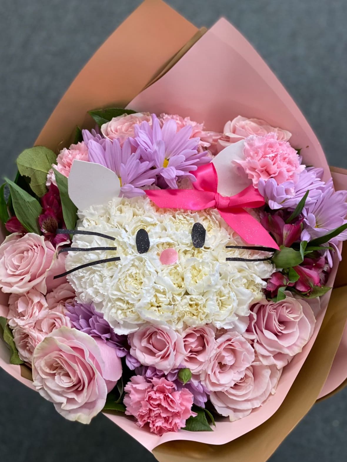 Pink and lavender bouquet with a cat-face flower center and ribbon