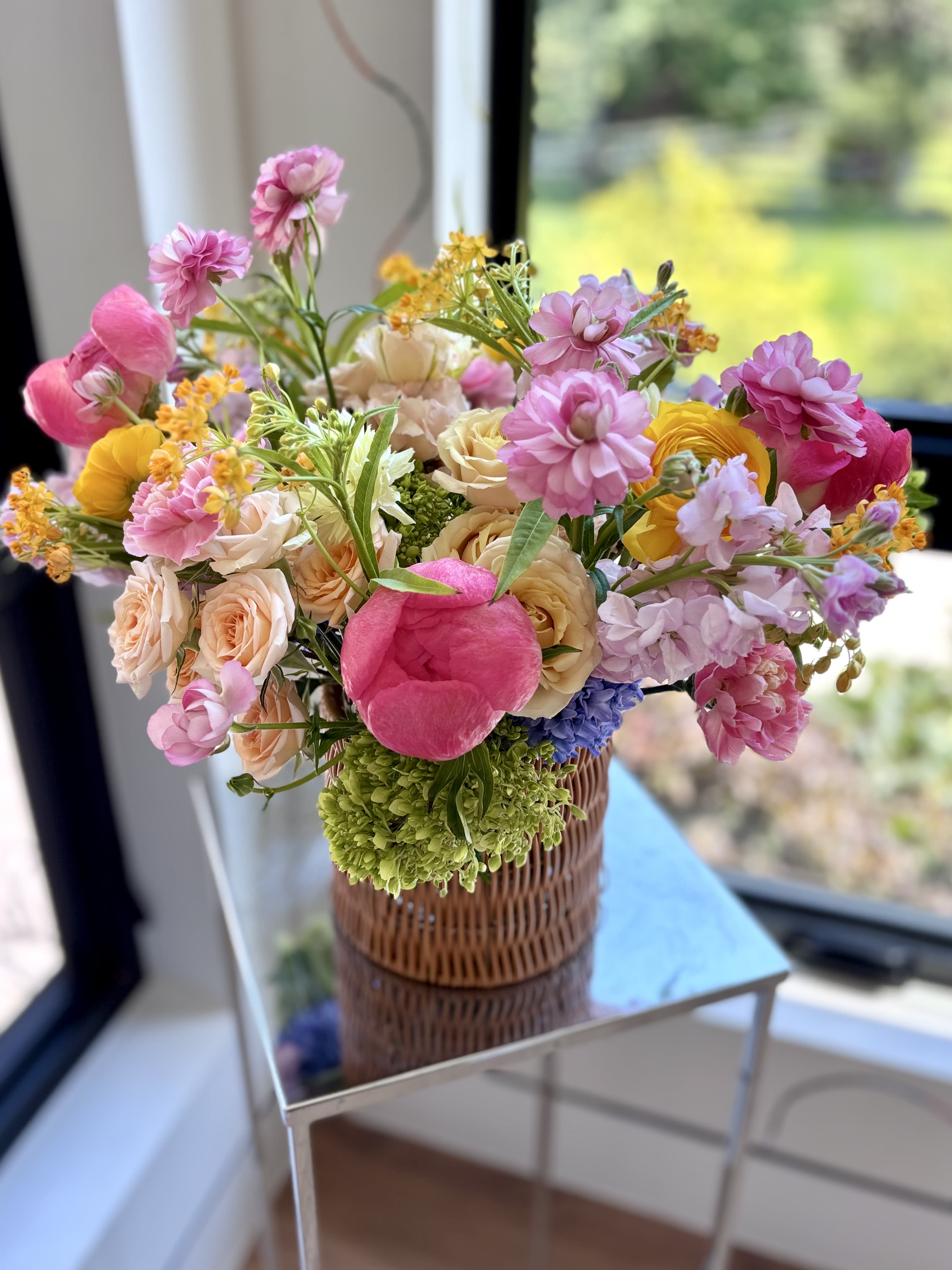 Peony Picnic - A joyful garden-style arrangement bursting with romantic pink blooms such as peonies, ranunculus and carnations, cheery yellow ranunculus, soft peach roses, lavender stock and clematis, with playful wildflower looking accents, all nestled in green hydrangeas. This bouquet brings the beauty of a blooming meadow indoors.