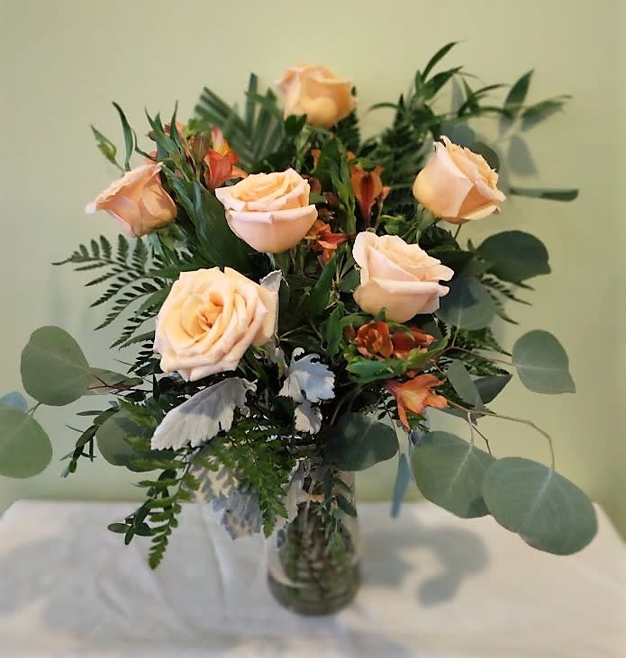 Peach roses in a glass vase with mixed greenery