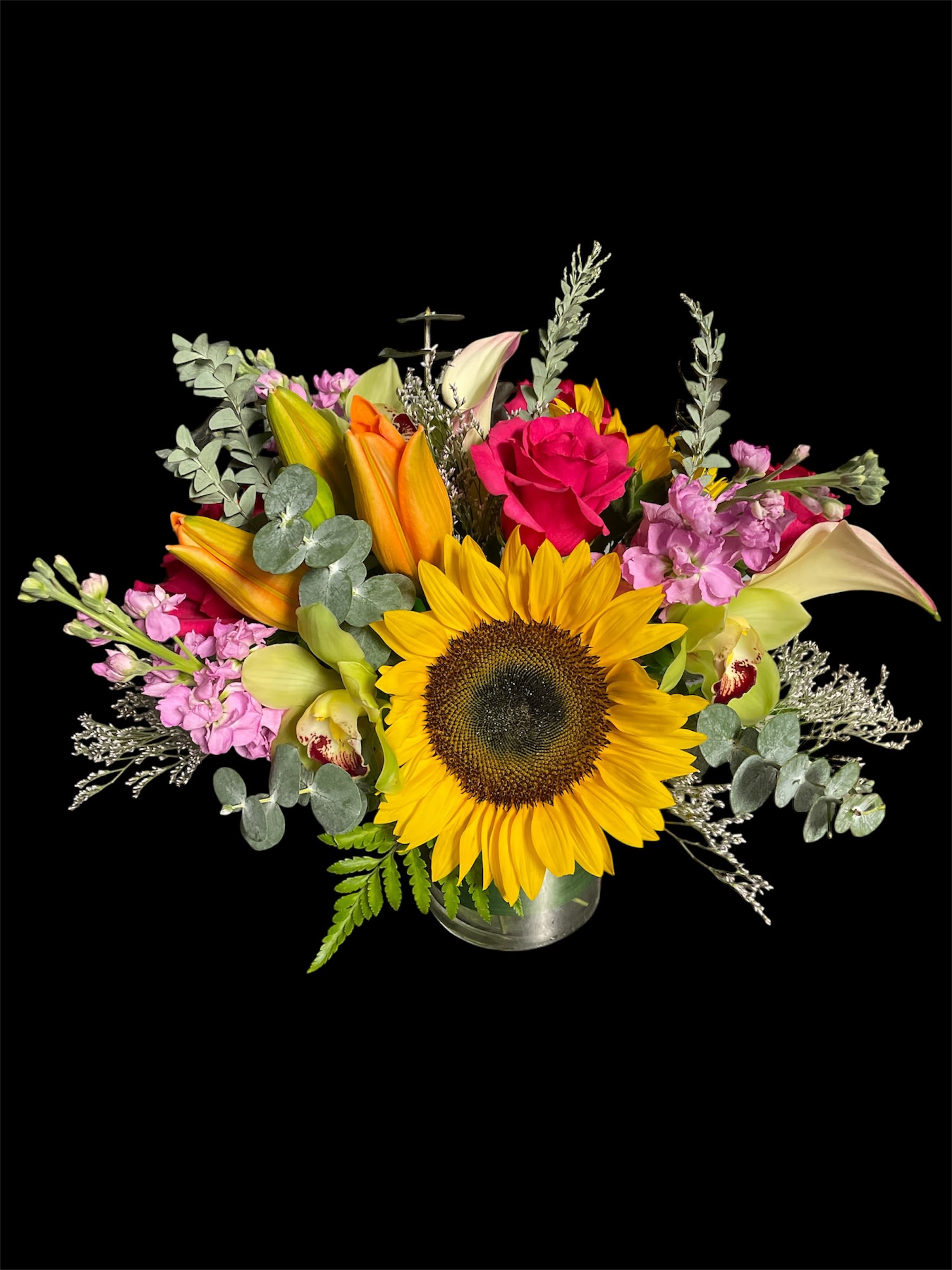 Sunshine symphony  - Brighten any day with this cheerful mix of sunflowers, roses, lilies, orchids, and lush greenery. Bursting with vibrant colors and natural charm, this arrangement is perfect for celebrating life’s joyful moments or simply bringing sunshine indoors.
