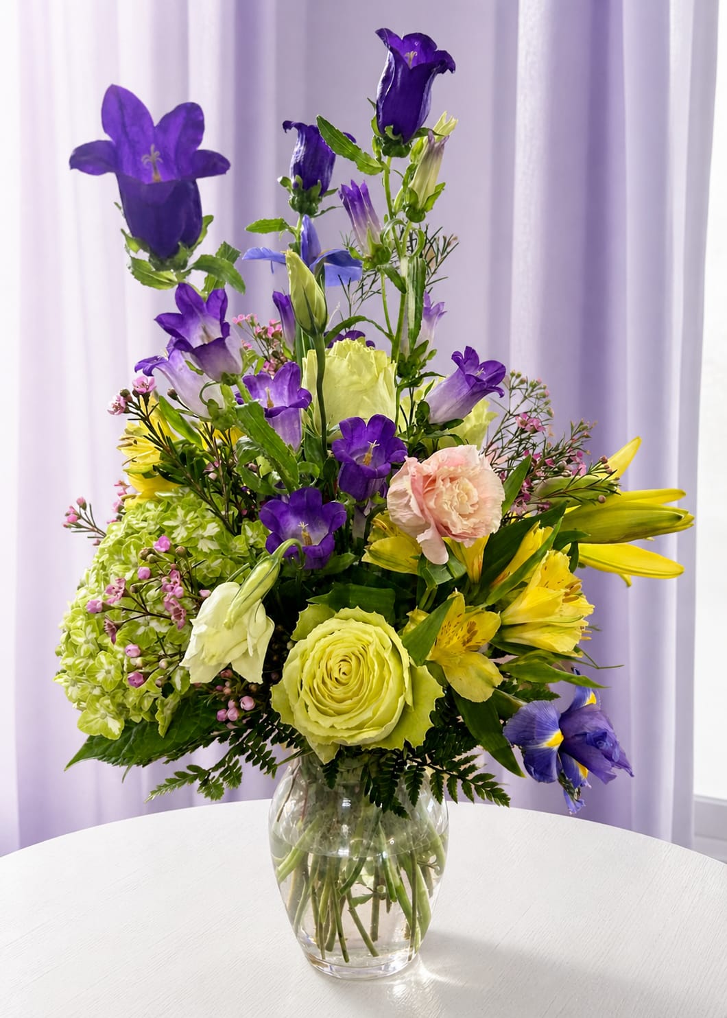  dreams spring  - Purple bell-shaped blooms reach skyward in this tall, garden-style flower arrangement, creating a lively vertical silhouette that feels like a spring breeze captured in glass. As a birthday bouquet or a cheerful congratulations arrangement, Lavender dreams is designed to make the recipient feel celebrated and noticed-the mix of purple, yellow, pink, and fresh greens reads bright and joyful without being fussy.  This mixed bouquet pairs Bells of Ireland for height with soft lisianthus, alstroemeria, carnations, and daisies gathered in a clear glass vase. The design features strong vertical lines over a dense, layered base so the taller purple flowers stand out while pale pinks and sunny yellows add contrast and soften the composition. Textures range from the bell-shaped blooms to ruffled carnations and delicate daisy petals for a full, garden-fresh look.  Perfect for birthdays, congratulations, or simply saying "I'm thinking of you," Lavender dreams suits anyone who appreciates a fresh, springlike palette and elegant height. Delivered in a clear glass vase, it's ready to display-keep flowers in fresh water, trim stems every few days, and place away from direct heat to extend enjoyment.  If any design elements are of major importance to your order, please include them in the florist instructions at checkout or contact us to ensure availability.