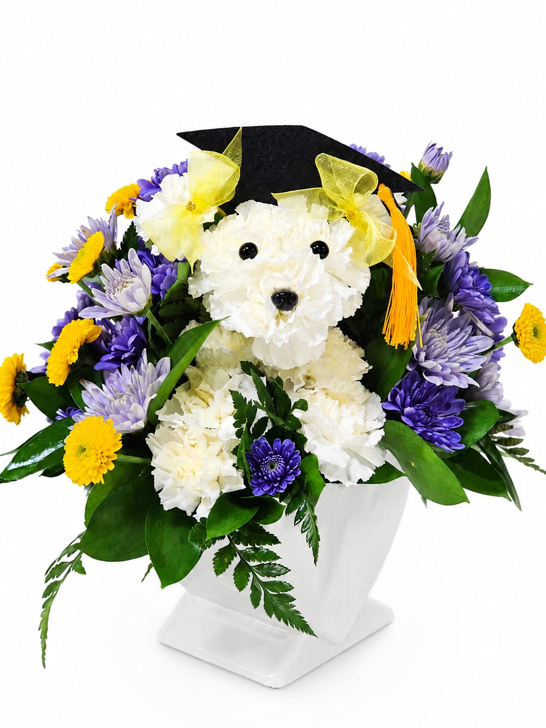 Graduation Puppy Floral Arrangement - Celebrate your graduate with this adorable handcrafted floral puppy arrangement! Designed with fresh white carnations, cheerful purple and yellow blooms, and topped with a graduation cap and tassel, this arrangement is the perfect gift for graduations, achievements, and special celebrations.   Features:  Handcrafted puppy made from fresh white carnations Purple and yellow seasonal flowers with lush greenery Decorative graduation cap with tassel and ribbon accents Arranged in a modern white ceramic vase Great for graduation parties, gifts, and photo displays