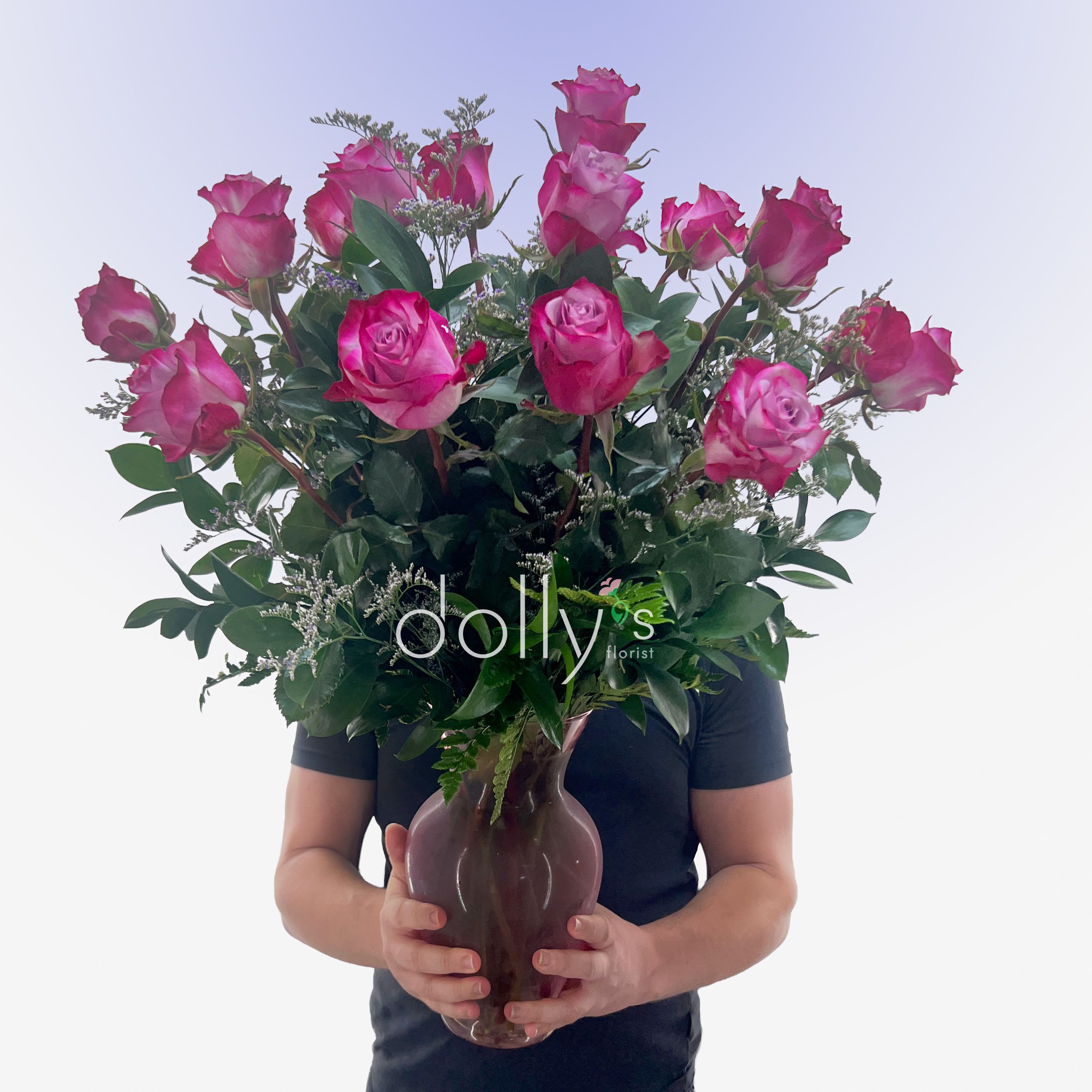 Classic 18 Magenta Roses - A lush cluster of magenta roses makes a joyful statement the moment it arrives-perfect as a birthday bouquet, anniversary roses, or a thoughtful thank-you arrangement. The rounded glass vase keeps the design feeling fresh and open, so the person you're celebrating will see those open blooms and buds at eye level and know you picked something special just for them.  Eighteen pink roses are arranged with abundant dark green foliage and delicate white-green filler to create a full, garden-like silhouette that reads romantic without being fussy. The mix of open roses and tighter buds gives pleasing texture and dimension, while the clear glass vase highlights the stems for a clean, classic look.  This arrangement suits a range of occasions when you want the recipient to feel noticed and cherished-whether marking an anniversary, brightening a birthday, or saying thanks. Delivered ready to display in the included vase; refresh the water every few days and trim stems to extend bloom life.
