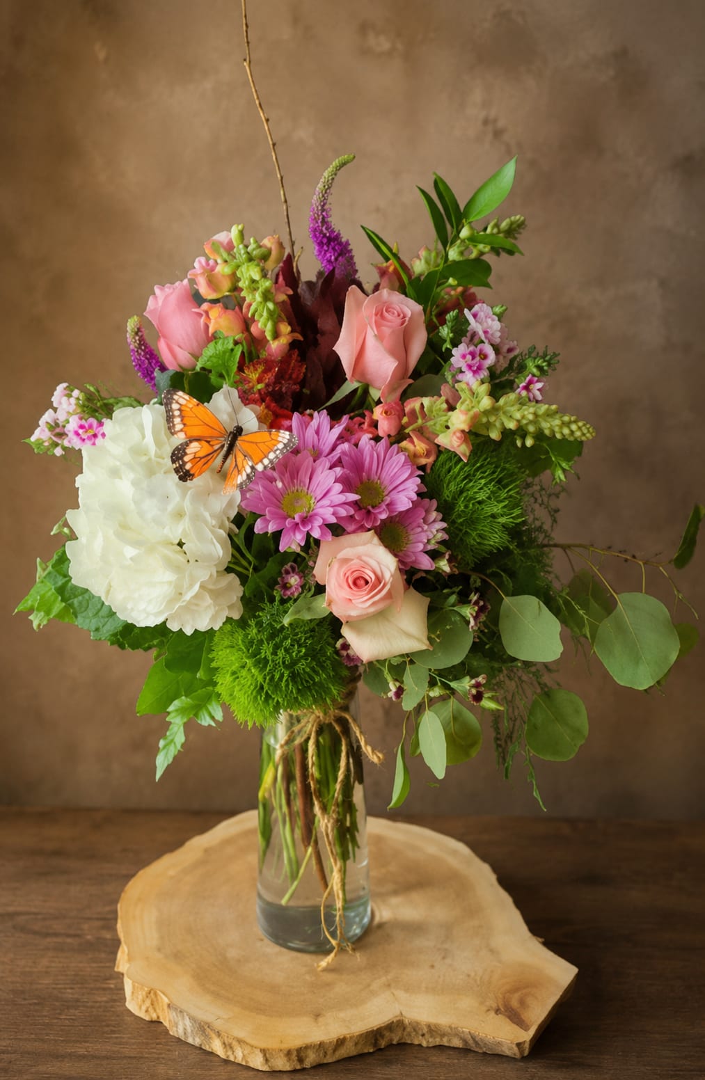 Mixed bouquet of pink and white flowers in a glass vase with a butterfly accent