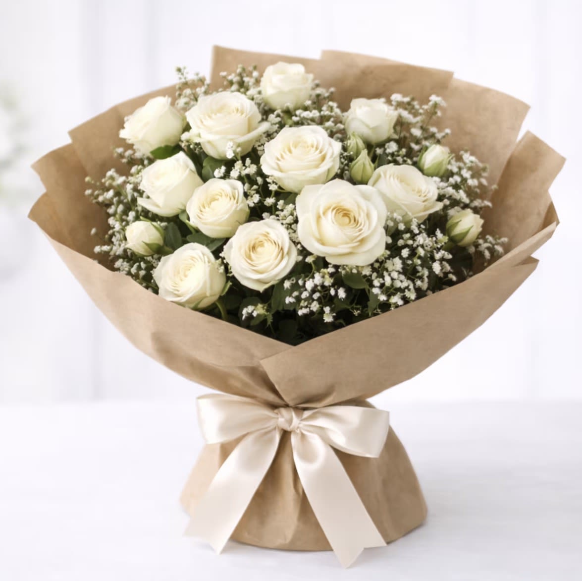 Pure Elegance by The Flower Spot™ - The arrangement features fresh white roses with delicate white filler blooms, wrapped in natural brown paper and finished with a wide ivory satin ribbon for a clean, understated presentation. The palette of white and green keeps the look timeless and versatile-equally suited to weddings, funerals, graduations, housewarmings, birthdays, get-well wishes, or simply saying "thinking of you." Each stem is curated by our designer and hand-tied to ensure a neat, long-lasting silhouette; bouquet size and care details are available at checkout so your recipient receives peak freshness.
