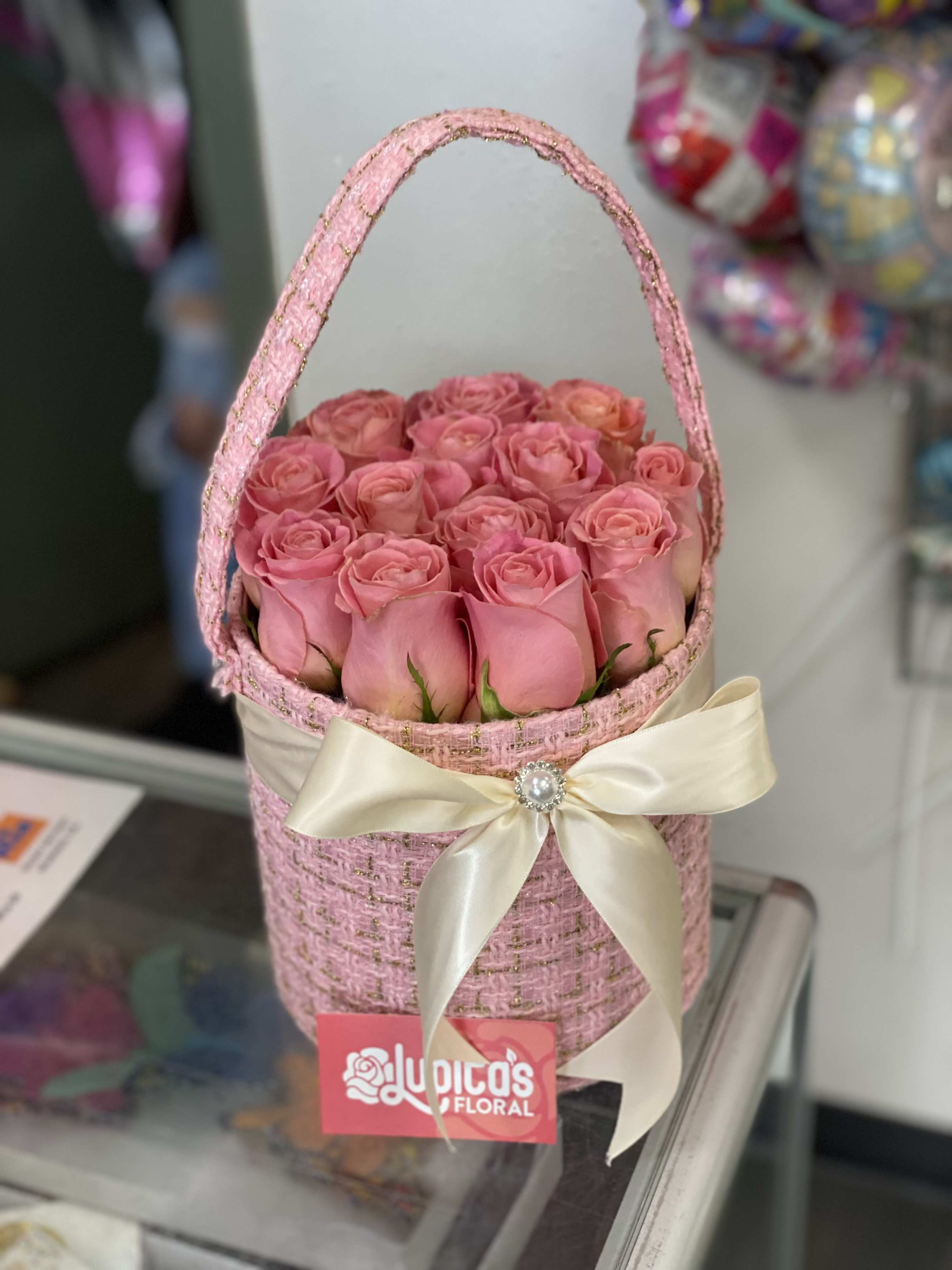 Pink roses arranged in a woven basket with a cream ribbon bow