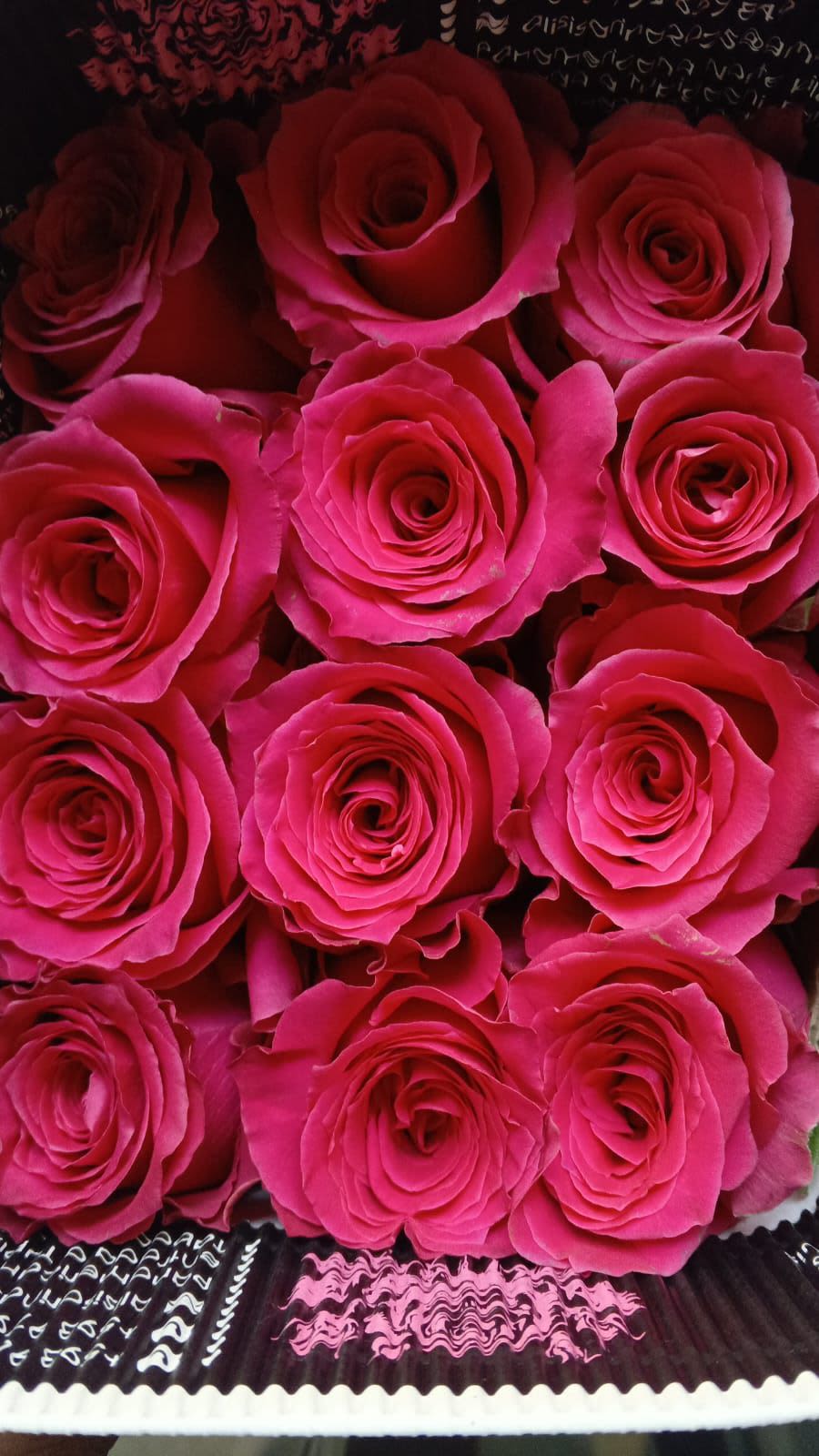 FLOWER MARKET, 25 LARGE ROSES - A lush, tightly packed rose arrangement that reads like a garden in full bloom - 25 large roses wrapped in decorative cardboard to create a bold, polished gift. Perfect as an anniversary or birthday bouquet, a romantic gesture for love and romance, or a striking "thank you" or "thinking of you" gift; its vivid color options also make it fitting for Mother's Day, Valentine's Day, graduations, housewarmings, and seasonal moments from spring through autumn (including Memorial Day and Thanksgiving displays).  Choose from rich red, classic white, soft light pink, hot pink, lavender, sunny yellow, or bright orange to tailor the mood: red for romance, white for sympathy or weddings, pinks for birthdays and new babies, lavender as a gentle "get well" or thinking-of-you choice, and yellow or orange for cheerful congratulations and summer events. The roses are arranged closely for a full, layered look and wrapped in dark patterned decorative paper that makes the petals pop - a presentation that reads as both romantic and polished.  It's a versatile choice for occasions from birthdays, anniversaries, and graduations to sympathy, retirement, and holiday gatherings; order with confidence for a meaningful, show-stopping gift that will make the recipient feel truly seen.