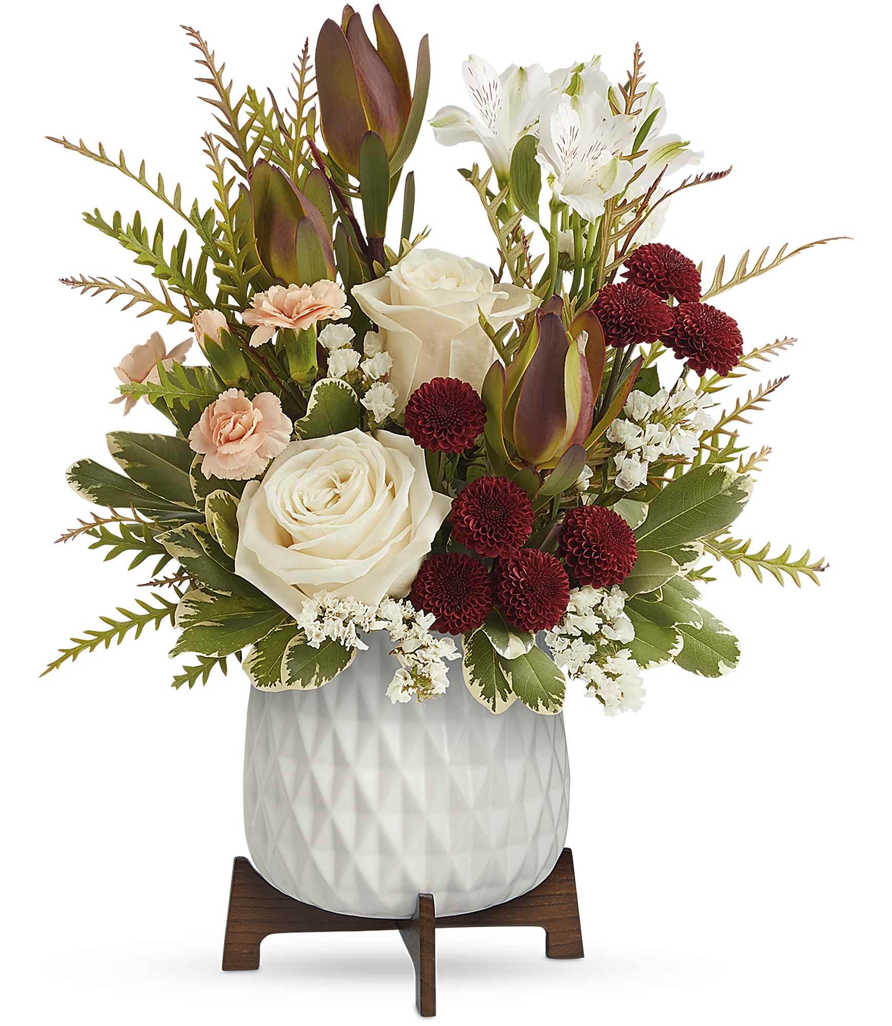 Timeless Treasure Bouquet - Brighten their day with Teleflora's Timeless Treasure Bouquet, showcasing radiant red and cream blooms presented in a sleek geometric ceramic planter atop a retro-inspired wooden base. It's an inspiring blend of elegance and nostalgia.  Experience refined beauty with a bouquet of cream roses, white alstroemeria, red leucadendron, peach carnations, and burgundy chrysanthemums. Accented by white sinuata statice, grevillea, and variegated pittosporum, this elegant arrangement is presented in Teleflora's Mid Mod Planter, epitomizing sophistication and style. Approximately 12 1/2" W x 15 1/2" H