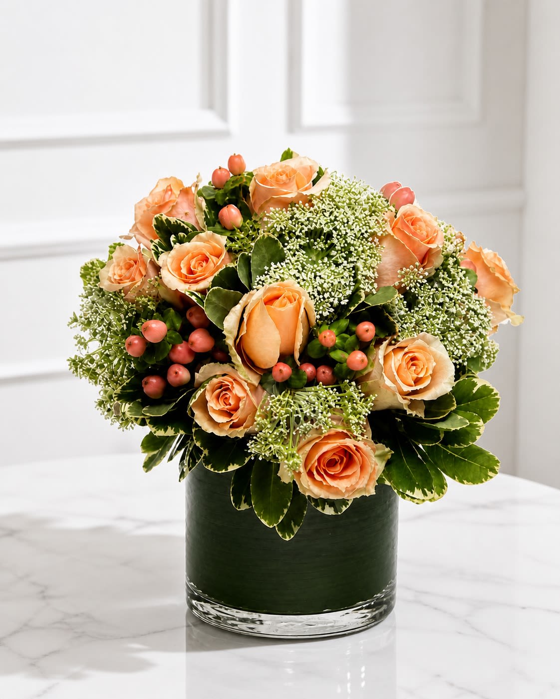 Desert Soleil - Warm, elegant, and garden-inspired, Desert Soleil is a refined floral arrangement designed with premium peach roses, seasonal textured blooms, soft berry accents, and layered greenery arranged in a modern leaf-lined cylinder vase. Inspired by warm desert tones and natural organic movement, this design blends softness and luxury into a timeless all-around presentation. The combination of creamy peach roses and airy green textures creates depth, warmth, and a sophisticated neutral palette that feels both fresh and elevated. Carefully arranged in a low contemporary cylinder vase lined with tropical foliage, Desert Soleil offers a clean modern look while maintaining a lush romantic garden feel. Perfect for birthdays, anniversaries, thank-you gifts, sympathy gestures, celebrations, or elegant everyday florals, this arrangement was designed for those who appreciate soft luxury and naturally beautiful floral styling. Seasonal substitutions may occur based on availability while maintaining the overall color palette, style, and luxurious garden-inspired aesthetic of the arrangement. Container substitutions of equal or greater value may also be used when necessary.