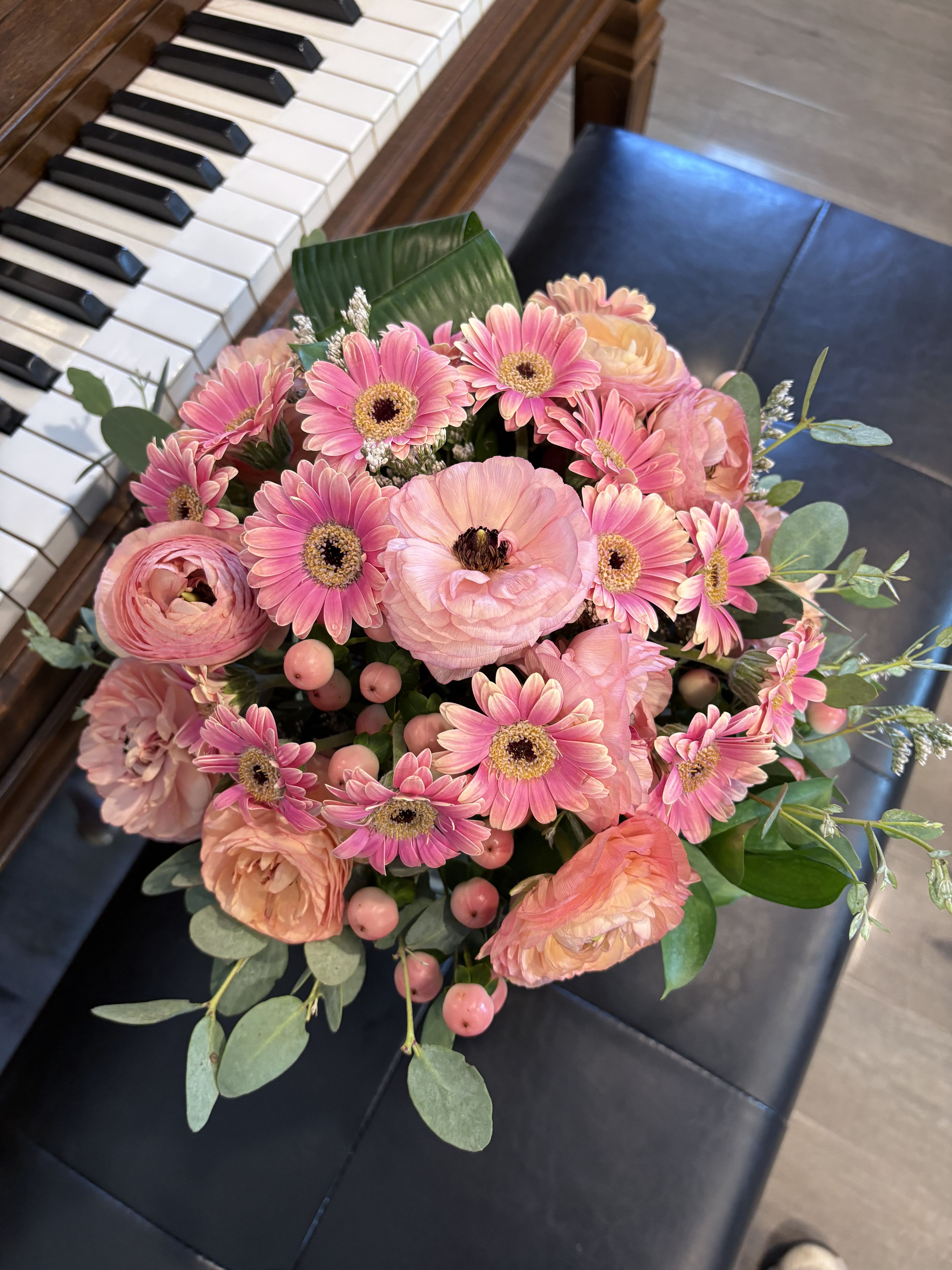 Peach bouquet - A lush cluster of pink gerbera daisies and soft peach ranunculus creates an instantly romantic peach bouquet perfect for a birthday bouquet, anniversary roses alternative, or a "just because" gift to show affection. The gentle mix of pink, peach, white, and green reads fresh and feminine-she'll feel noticed and celebrated the moment she sees it.  This hand-tied arrangement is full and rounded, with dense blooms of gerbera daisies and blush ranunculus accented by round pink berries and airy eucalyptus for texture and movement. The garden-style composition feels intimate and elegant without being fussy, pairing soft petal textures with cool green foliage for a balanced, natural look.  Send this to a close friend, mother, or partner to mark a celebration or to brighten their day; it's the kind of bouquet that feels thoughtfully chosen and immediately uplifting. Care is simple-trim stems and place in fresh water to enjoy the blooms for several days.