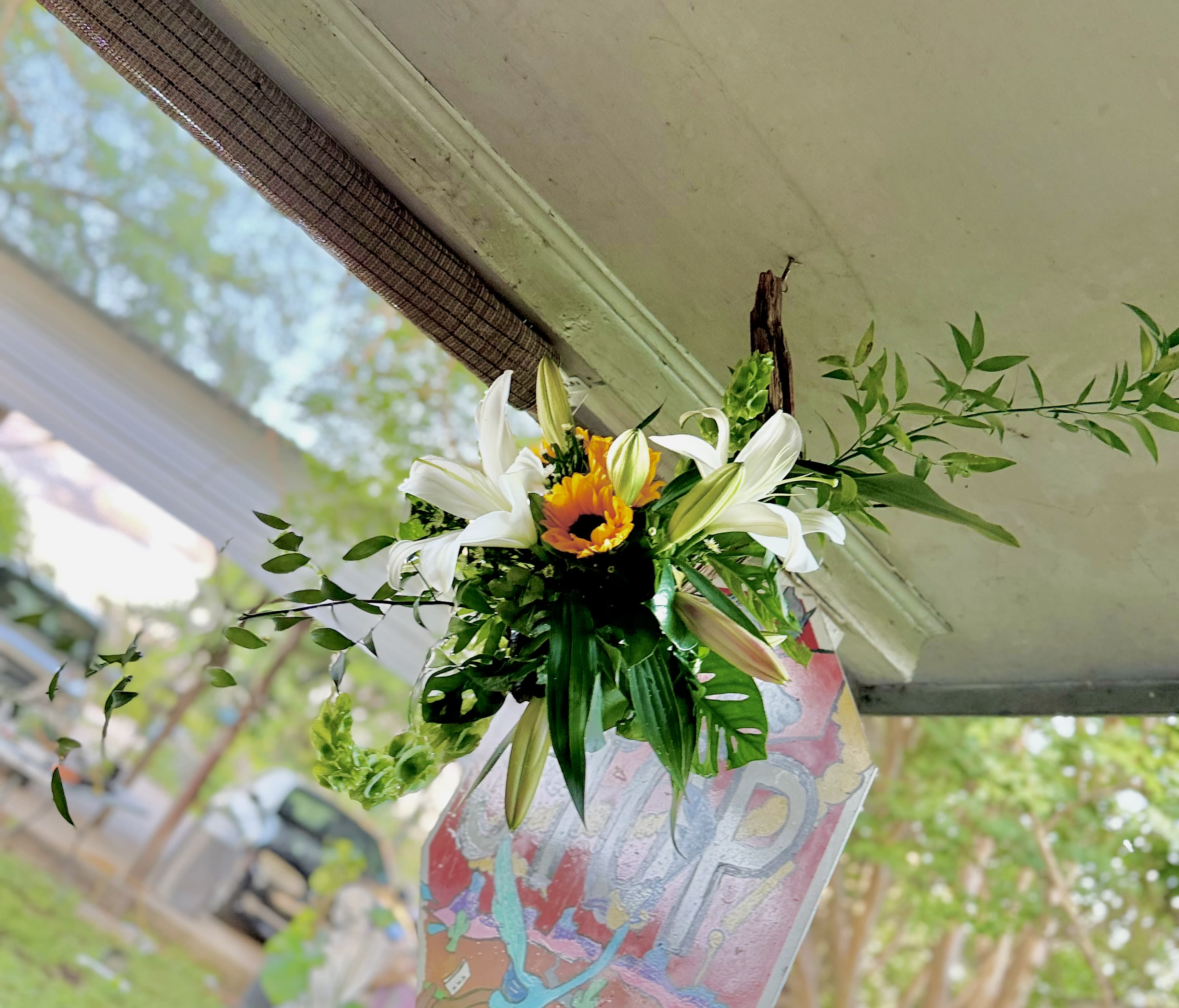 Verdant Halo - A Custom Living Art Design by Wonderland Flowers - A sculptural hanging floral piece featuring unopened lilies, cascading bells of Ireland, and lush tropical greens wrapped around natural driftwood. Organic, modern, and quietly dramatic. 
