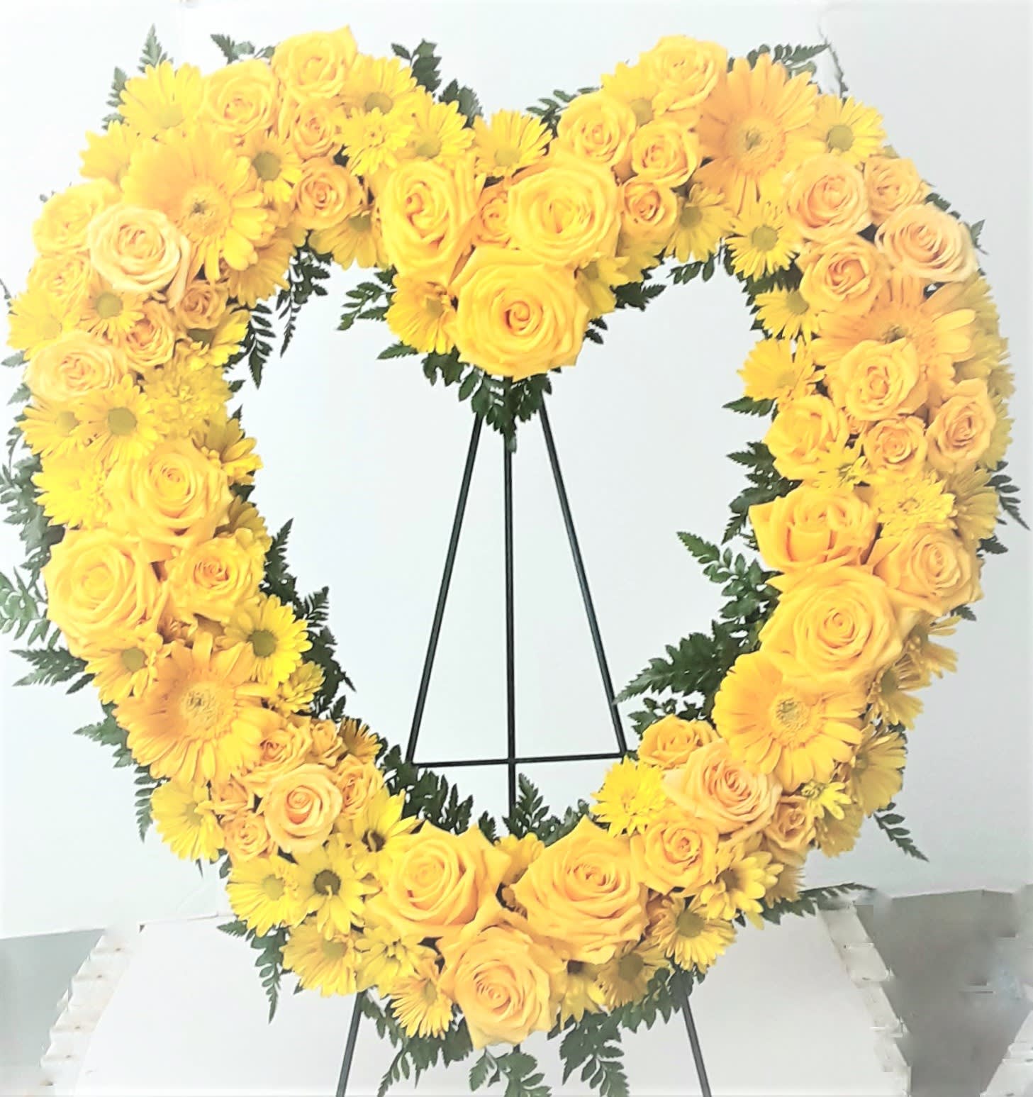 Yellow rose and daisy heart wreath on a black stand