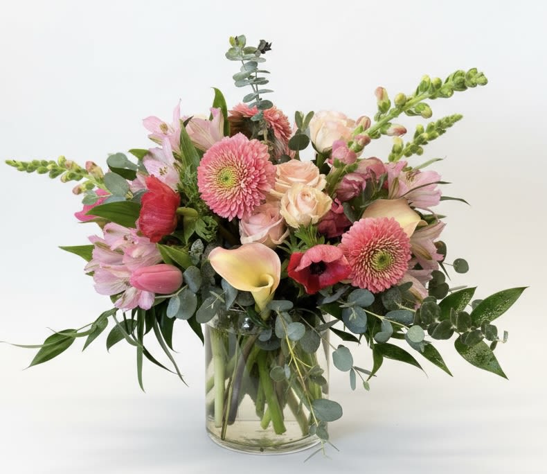 Amelia - A lush, romantic bouquet that reads like a springtime garden-Amelia is a flower arrangement perfect for birthdays, thank you gestures, or just because. The mix of pink, blush, peach and pops of hot pink creates an uplifting, celebratory mood the person you're thinking of will notice the moment it arrives.  This design combines large gerbera daisies, elegant calla lilies, classic roses, cheerful tulips, delicate alstroemeria and tall snapdragon spikes for an airy, textured silhouette. Soft gray-green eucalyptus and foliage tuck around the stems to balance the warm palette and keep the composition feeling fresh. Stems are gathered in a clear glass vase for a clean, modern presentation that shows off the natural lines and height of the flowers.  Choose Amelia when you want someone to feel warmly celebrated-bright, hopeful, and truly seen. The arrangement arrives ready to display; refresh the water and trim stems every few days to extend bloom life.