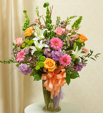 Mixed bouquet with pink gerberas, roses, lilies, and purple flowers in a glass vase