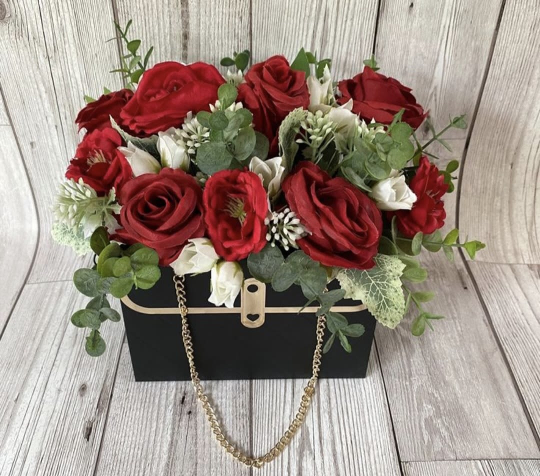 Red roses and white blooms arranged in a black box with a gold chain handle.